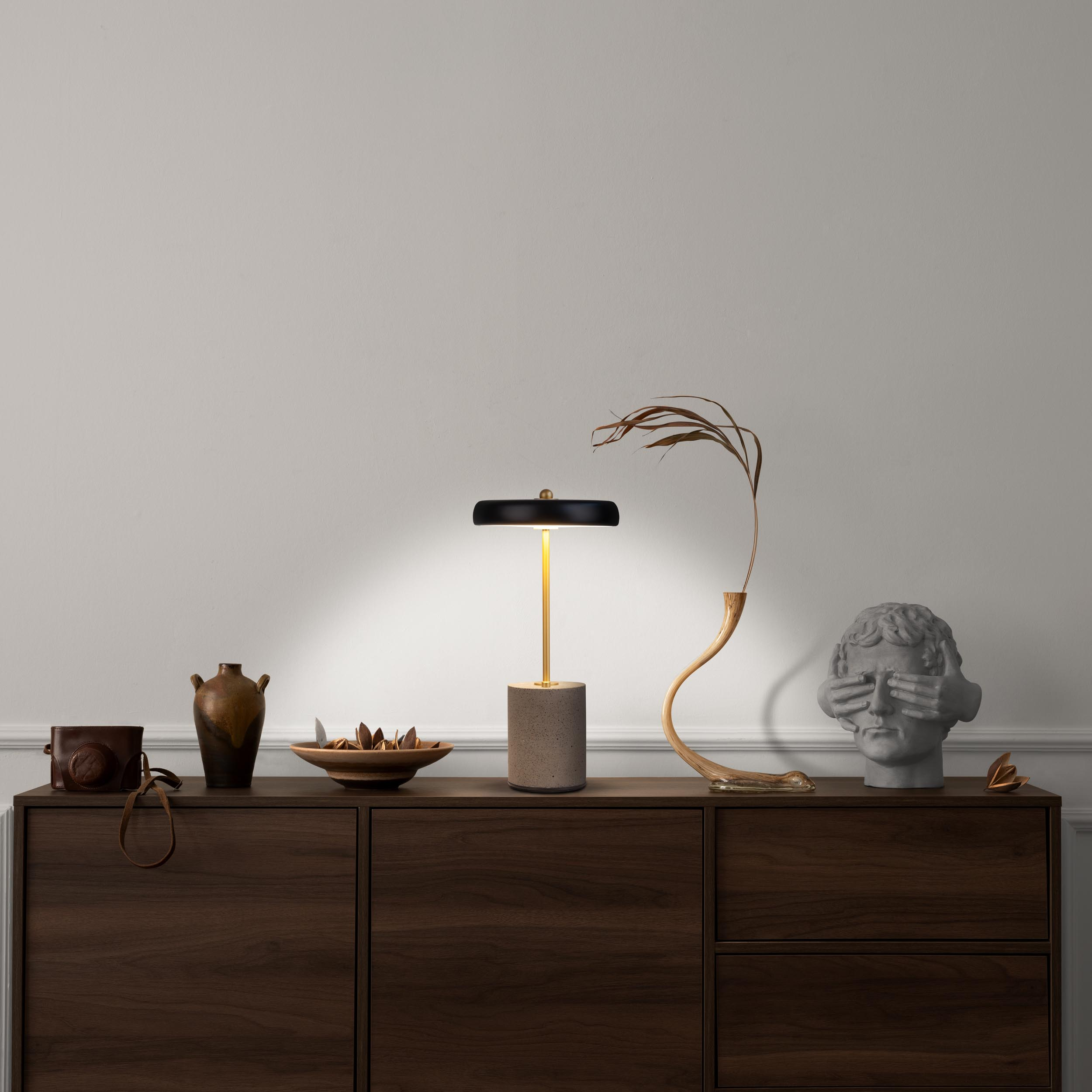 Stilvolle Tischlampe auf dunklem Holzschrank mit Deko. Licht scheint von oben.