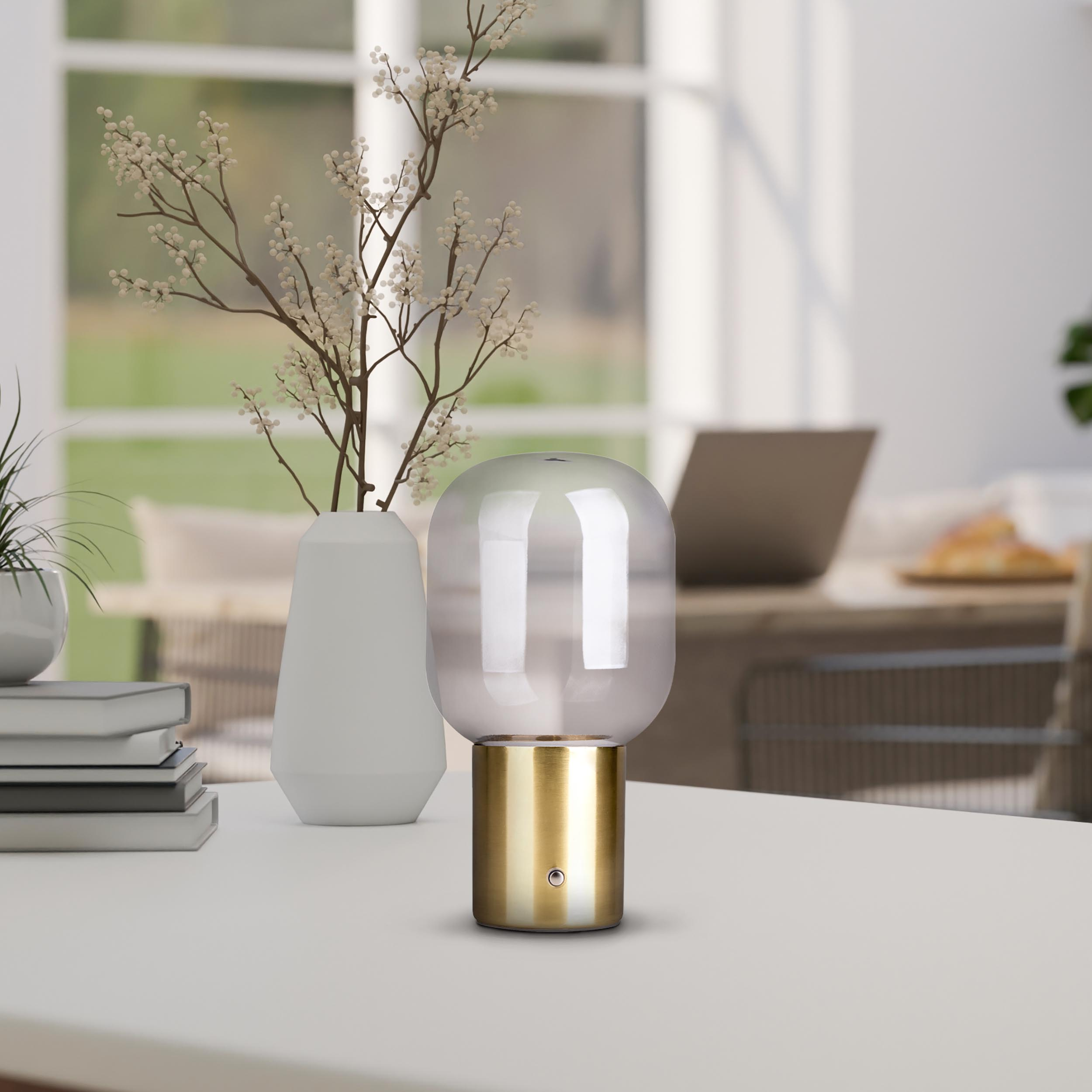 Eine moderne Lampe mit goldenem Sockel, eine weiße Vase mit einer Blume und ein Laptop.
