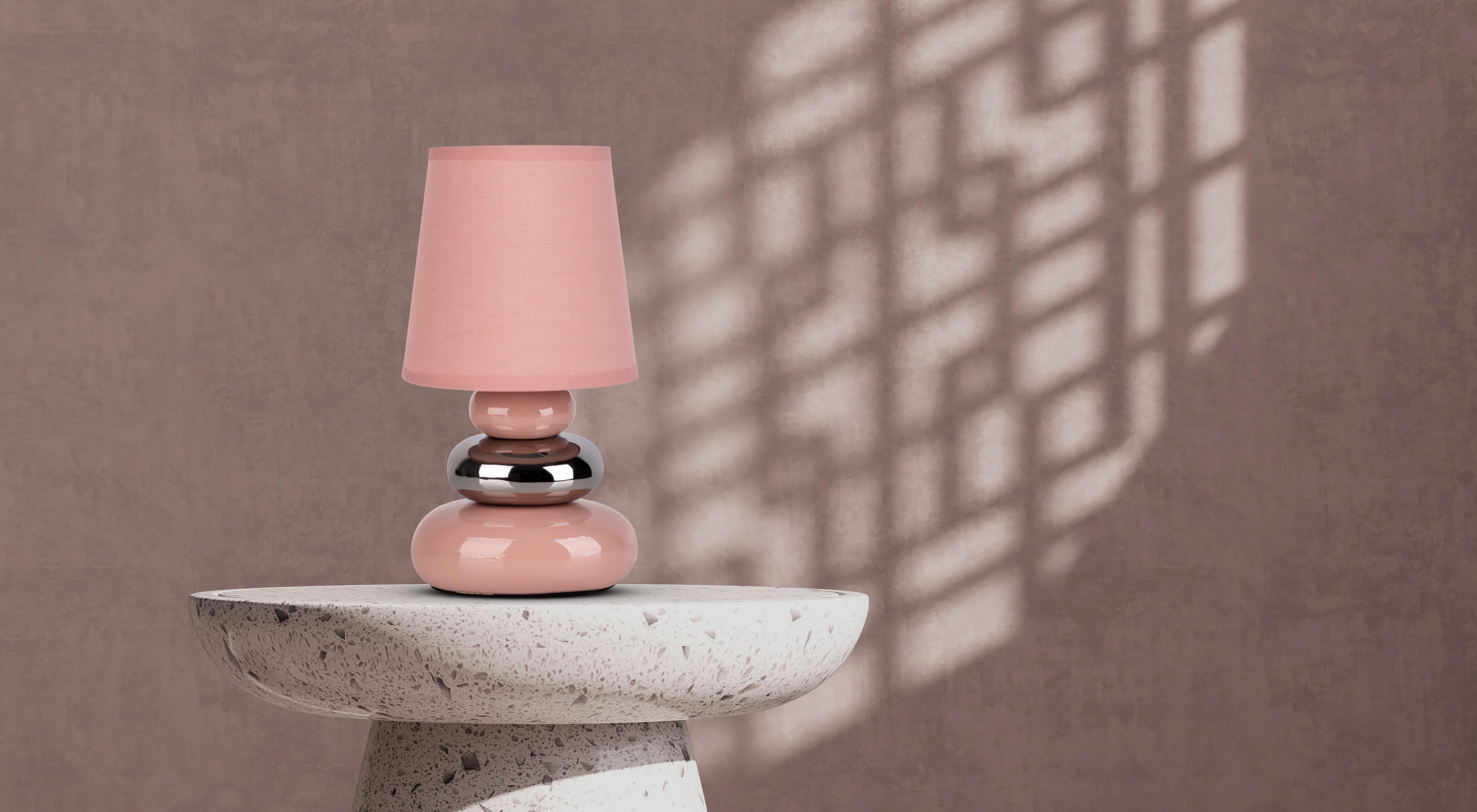Eine rosa Lampe auf einem Steintisch mit Schatten an einer braunen Wand.