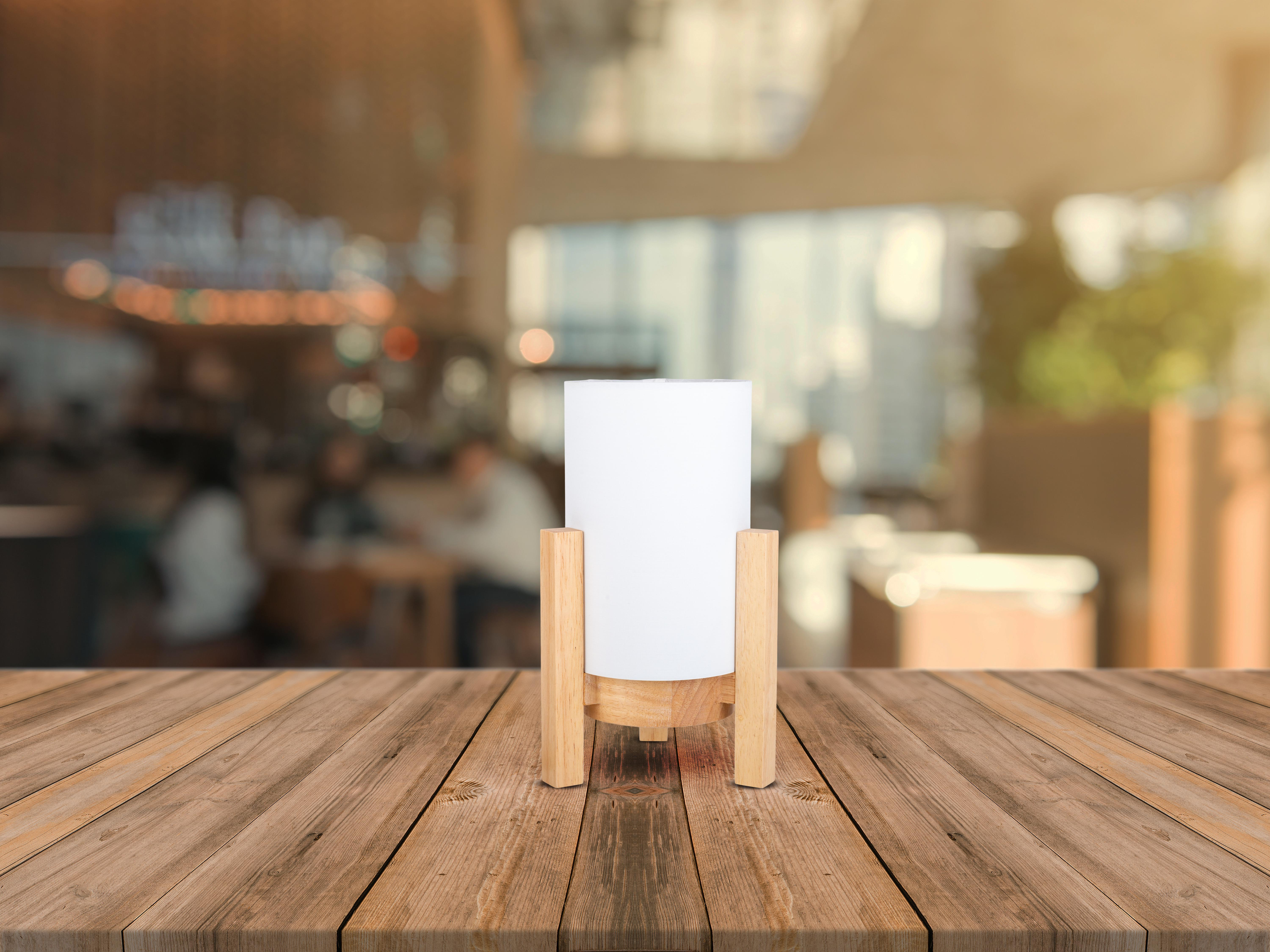 Weiße Lampe auf Holzständer, auf Holztisch, mit verschwommenem Café-Hintergrund.