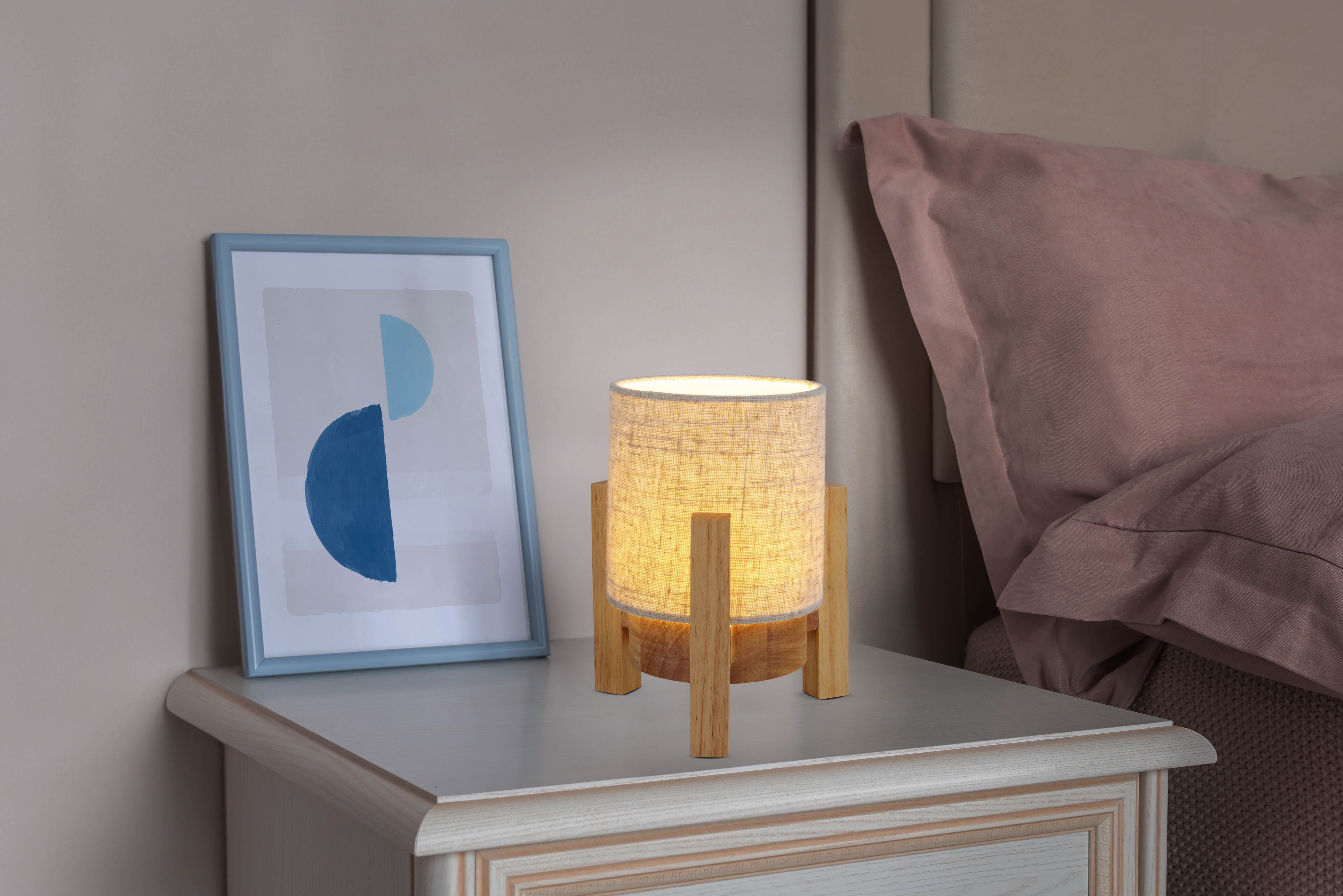 Nachttisch mit Lampe und Bilderrahmen. Lampe hat Holzfuß und beigen Schirm. Blaue Kunst.