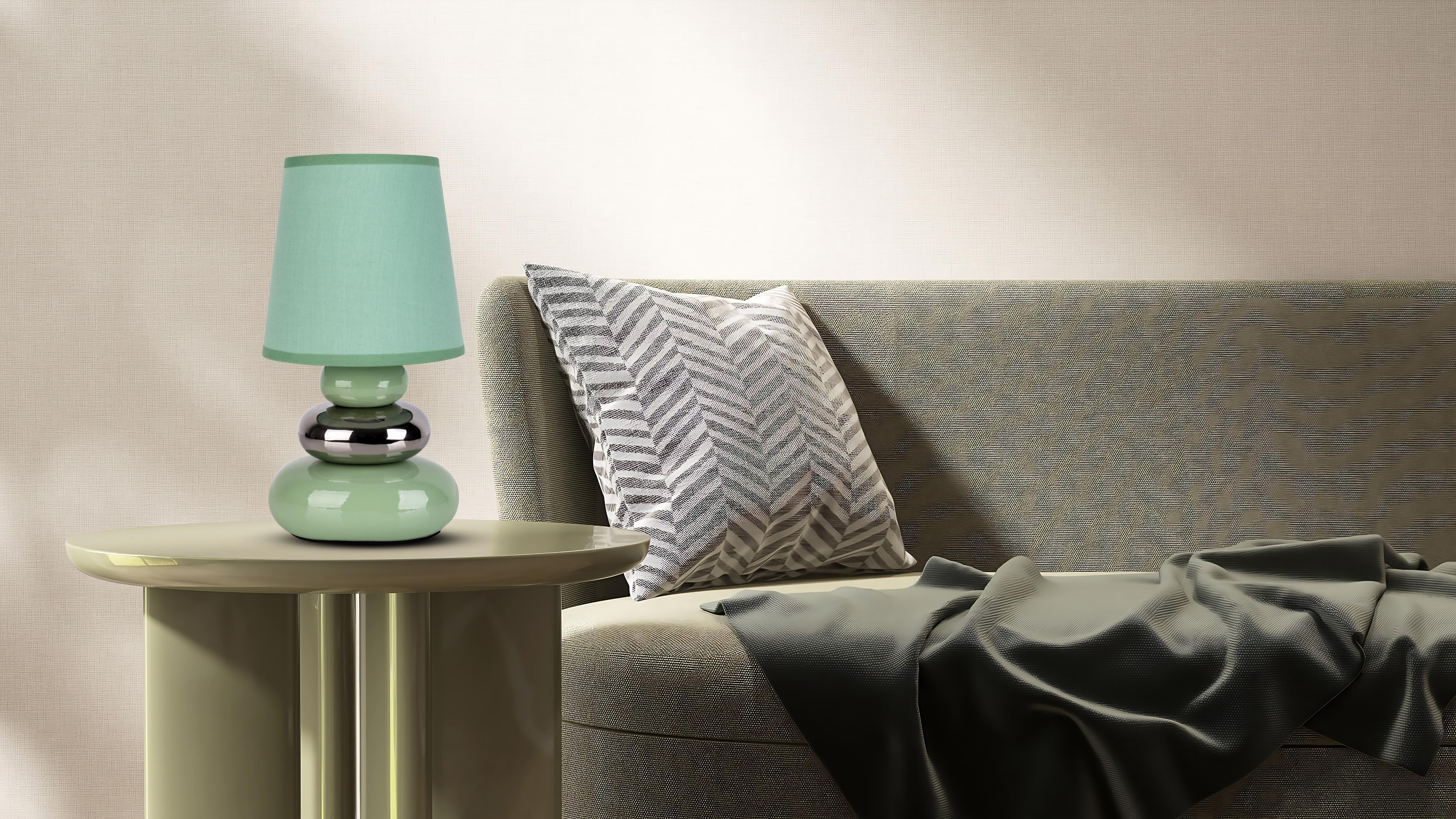 Eine mintgrüne Lampe auf einem runden Tisch, mit Kissen und Decke.
