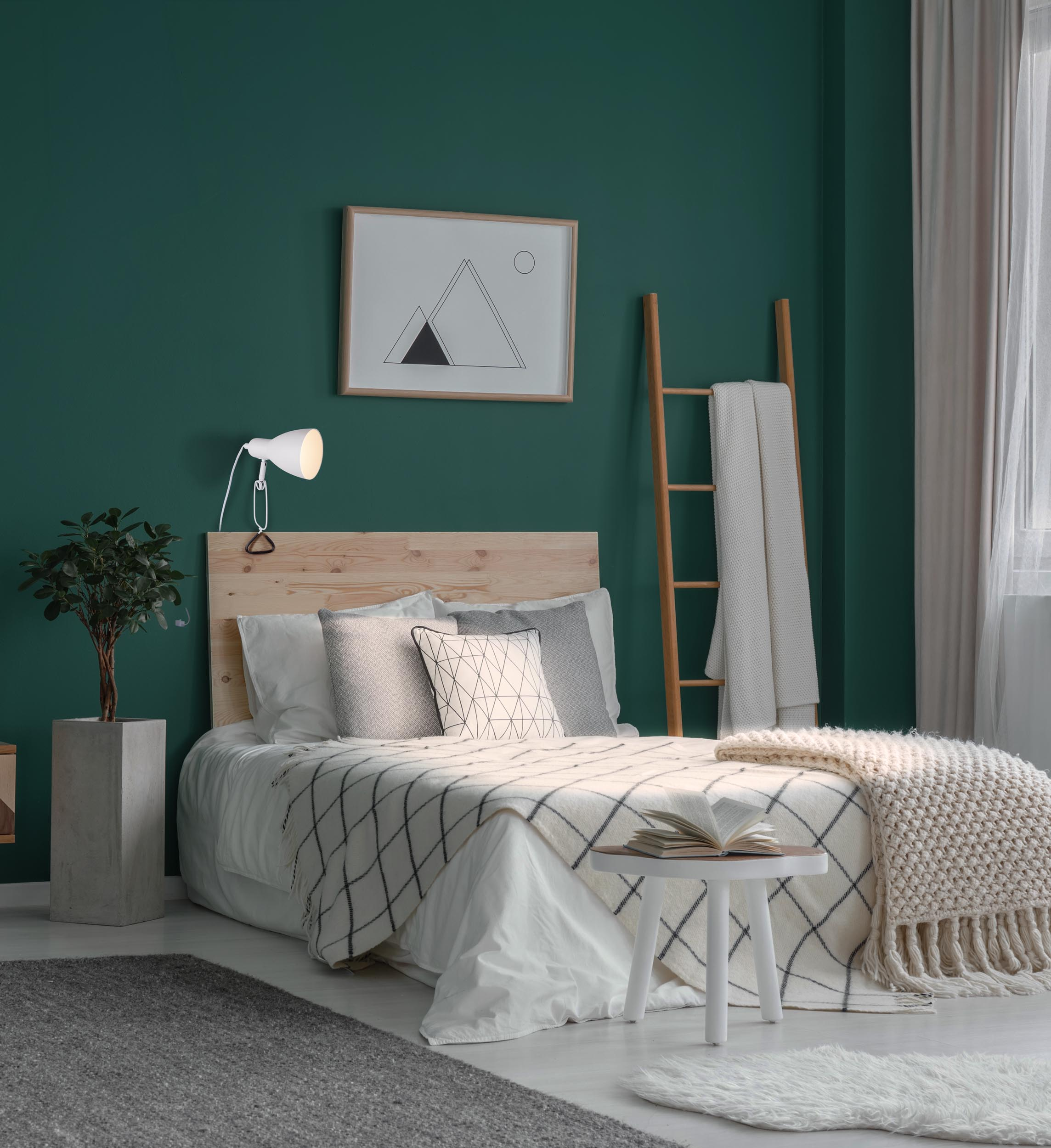 Schlafzimmer mit grüner Wand, Bett mit gemusterter Decke, Holz-Kopfteil und weißer Lampe.