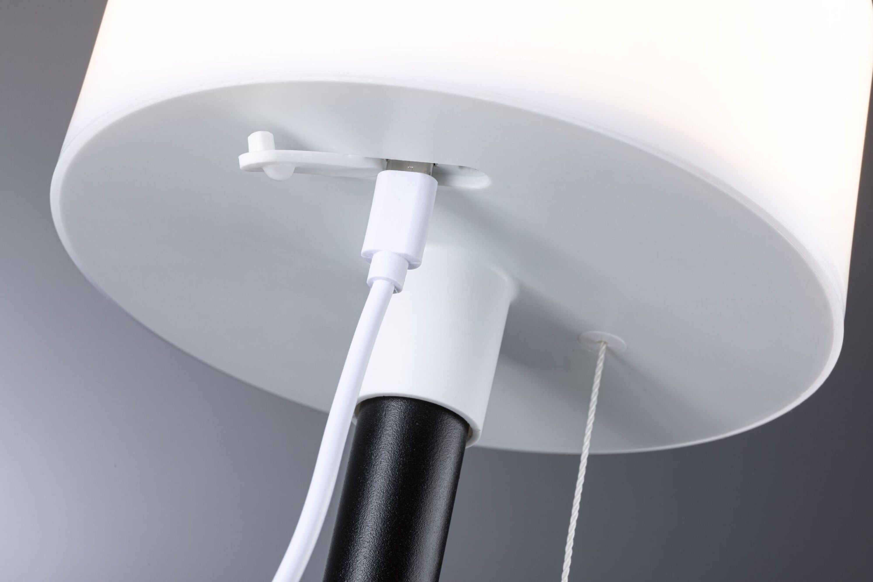 Zbliżenie podstawy lampy z kablem USB i sznurkiem, wszystko białe i czarne.