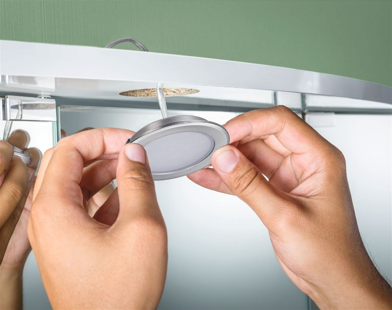 Ręce instalujące srebrną oprawę oświetleniową LED w lustrzanej powierzchni.