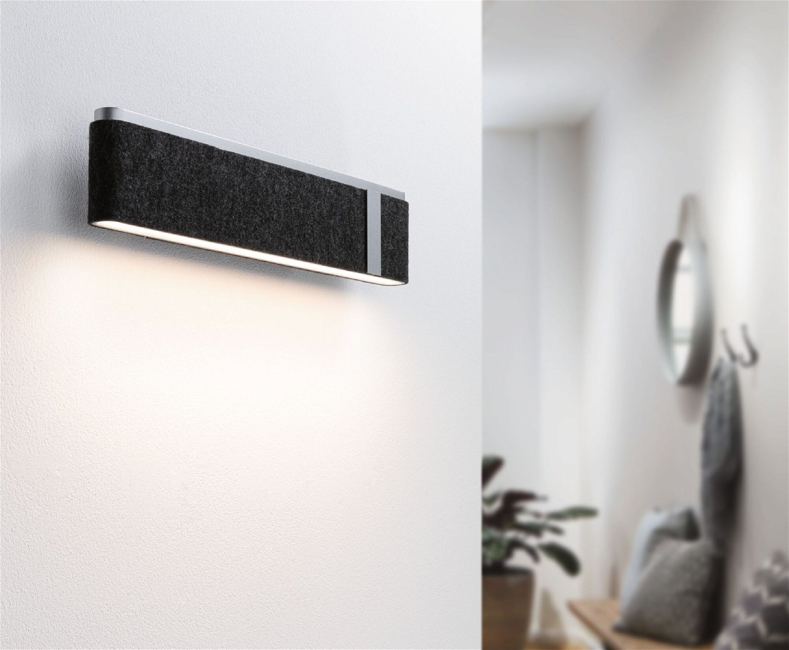 Lampa ścienna z czarną osłoną z tkaniny i srebrną obwódką. Jest zapalona.