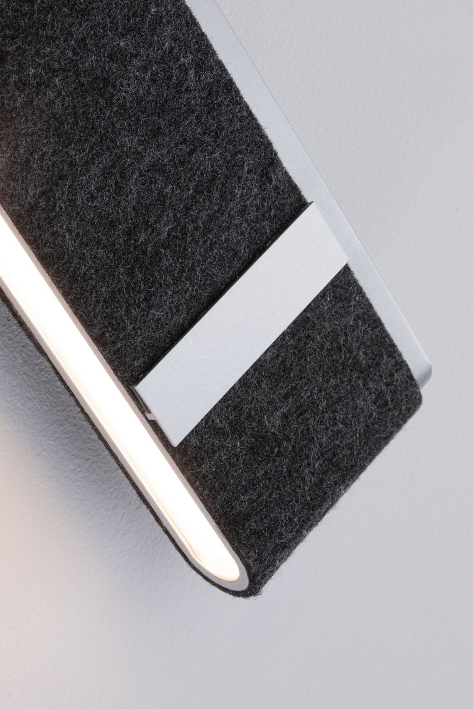 Zbliżenie na lampę ścienną. Oprawa jest szara z ciemnoszarą filcową osłoną.