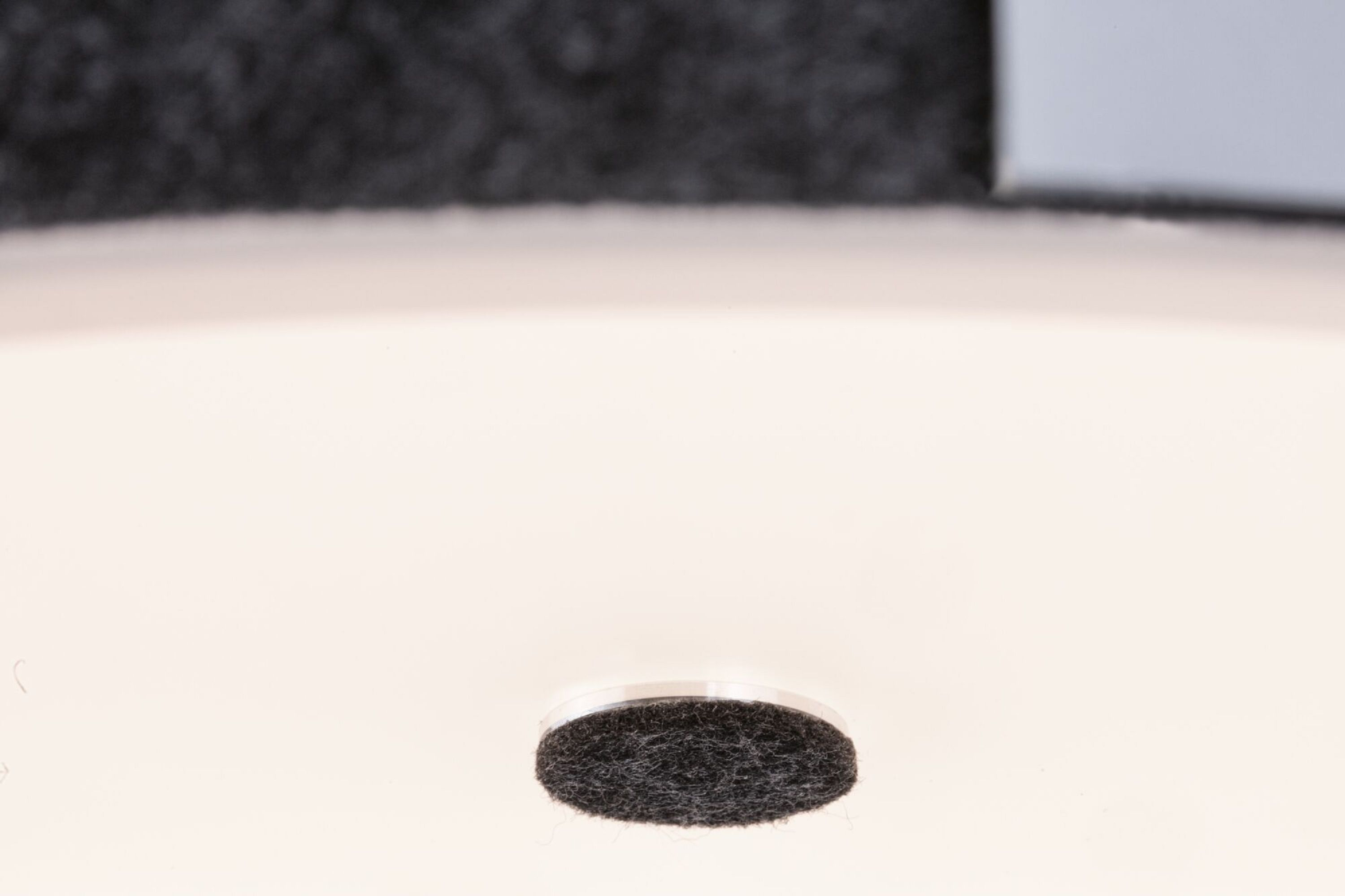 Mała, okrągła, czarna podkładka filcowa przyklejona do białej powierzchni, ujęcie z bliska.