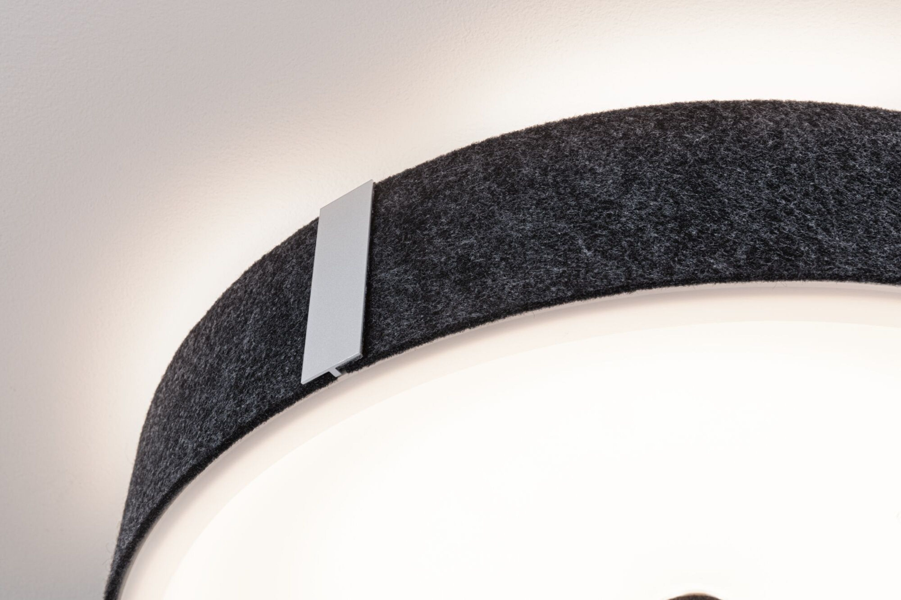 Zbliżenie okrągłej lampy sufitowej z ciemnoszarą filcową obwódką i białym obszarem światła.