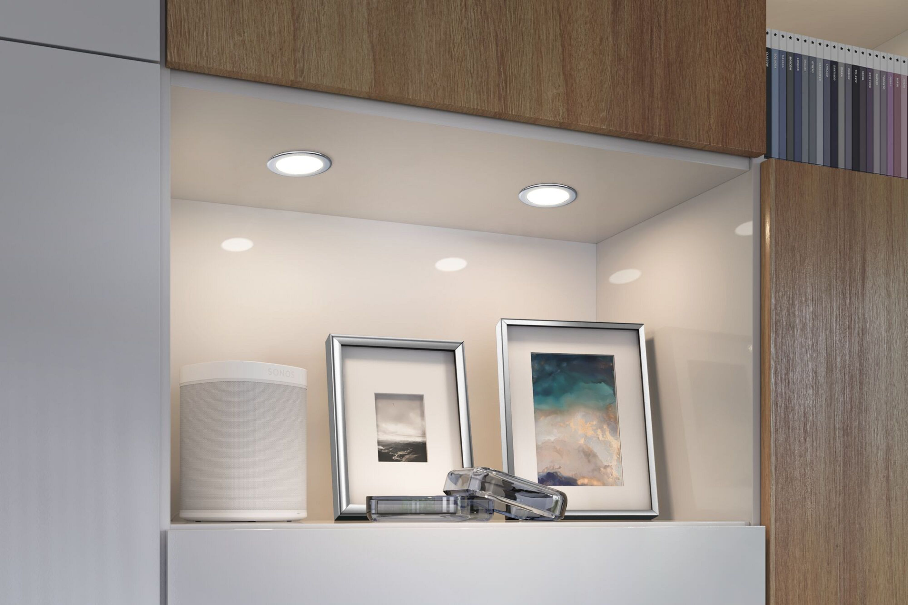 Półka z dwoma wpuszczanymi światłami, głośnikiem i dwoma oprawionymi zdjęciami na białej ścianie.