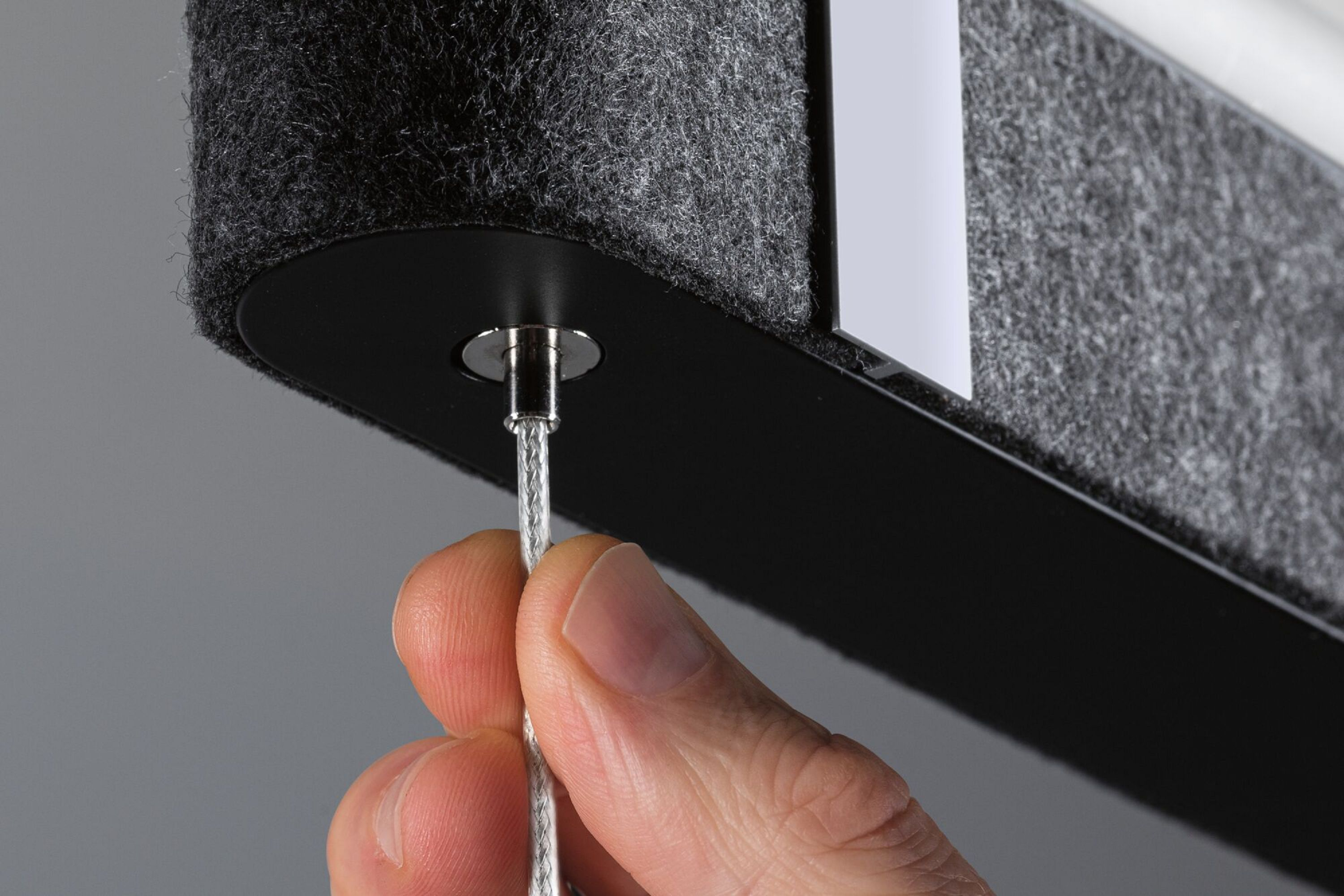 Dłoń trzymająca kabel, podłączając go do ciemnoszarego panelu filcowego.