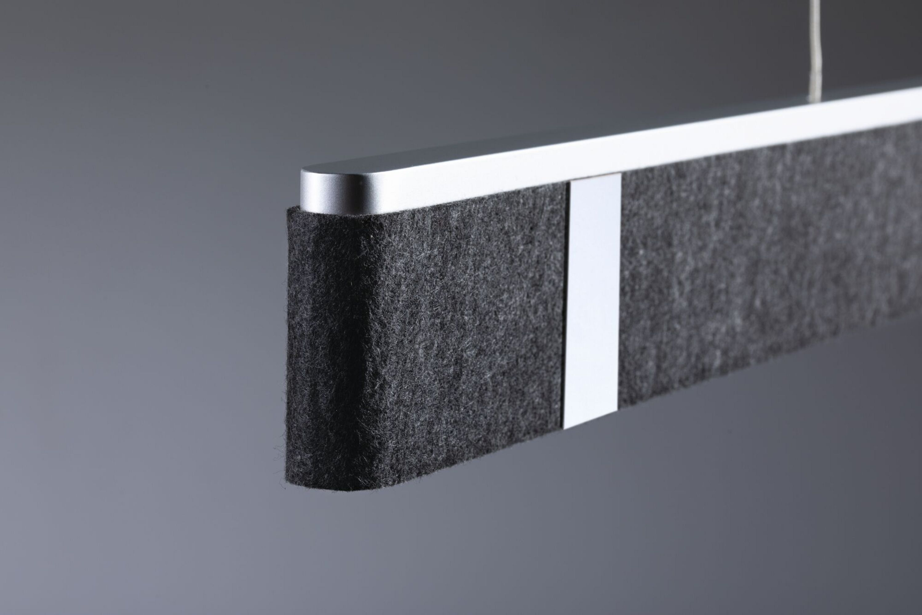 Zbliżenie nowoczesnej lampy liniowej z ciemnoszarym filcowym wykończeniem.