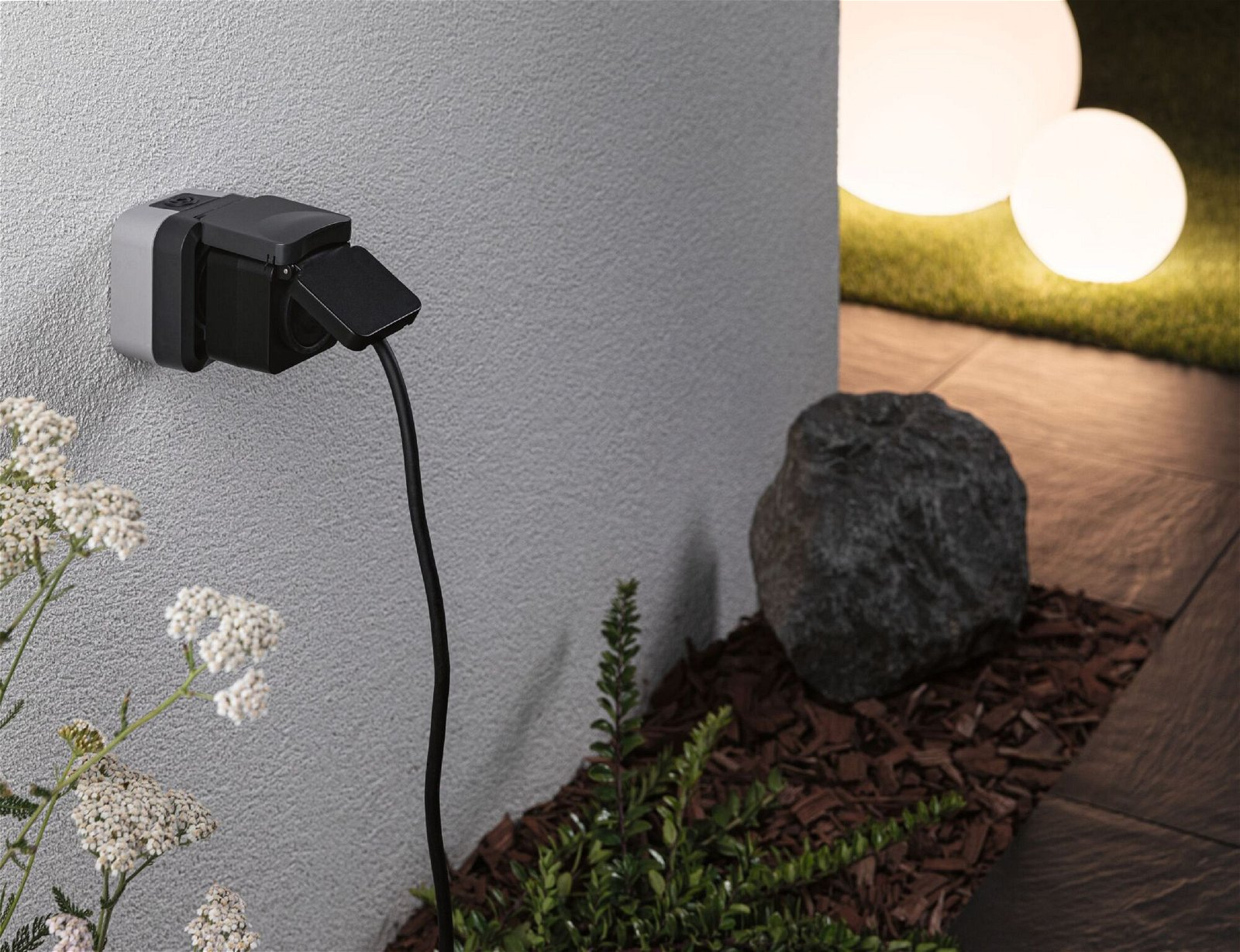 Zewnętrzne gniazdo elektryczne na teksturowanej ścianie z elementami ogrodu.