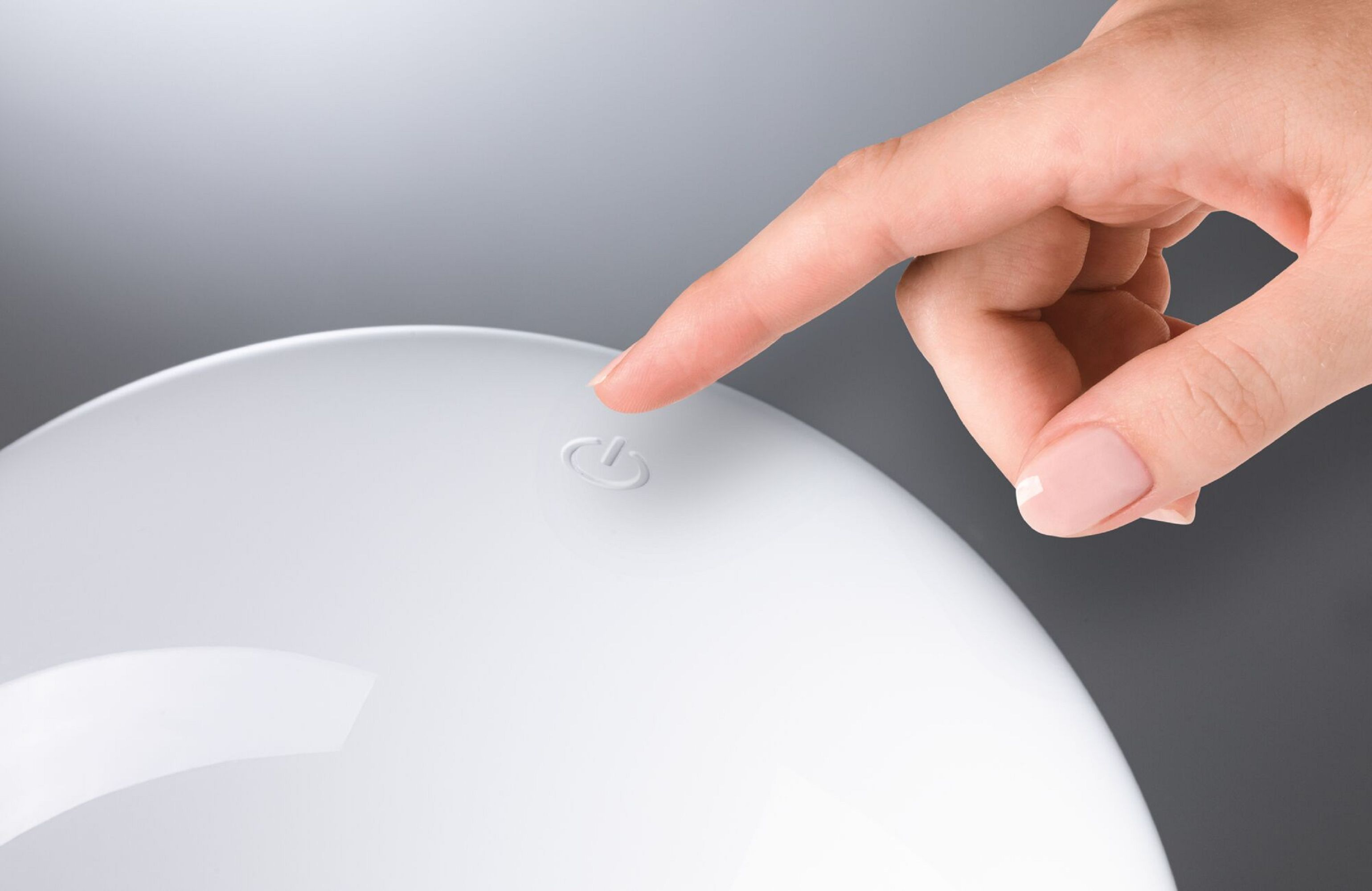 Ręka naciska biały przycisk zasilania na białym urządzeniu.