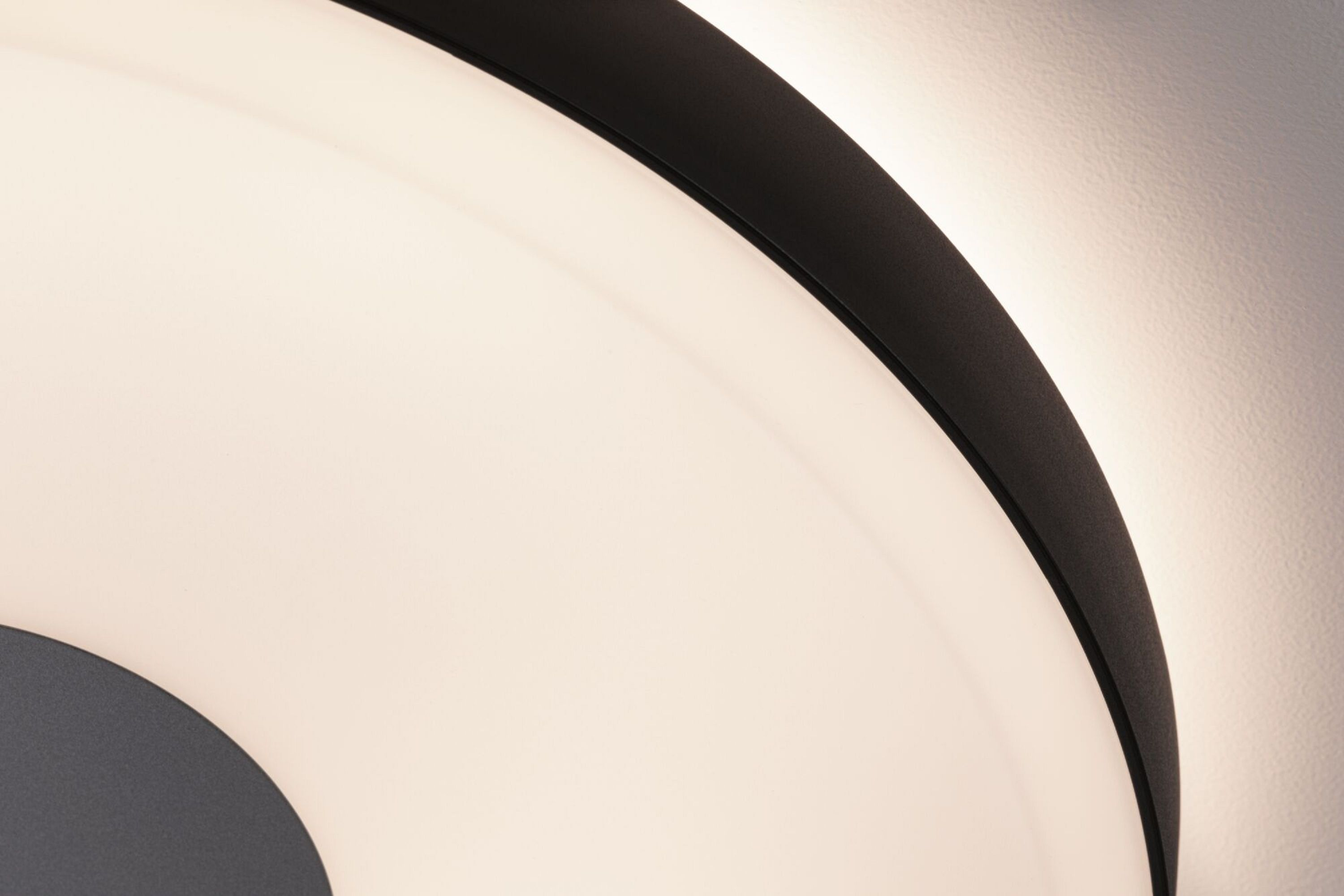 Zbliżenie nowoczesnej, czarno-białej okrągłej lampy sufitowej z jasnym, białym światłem.