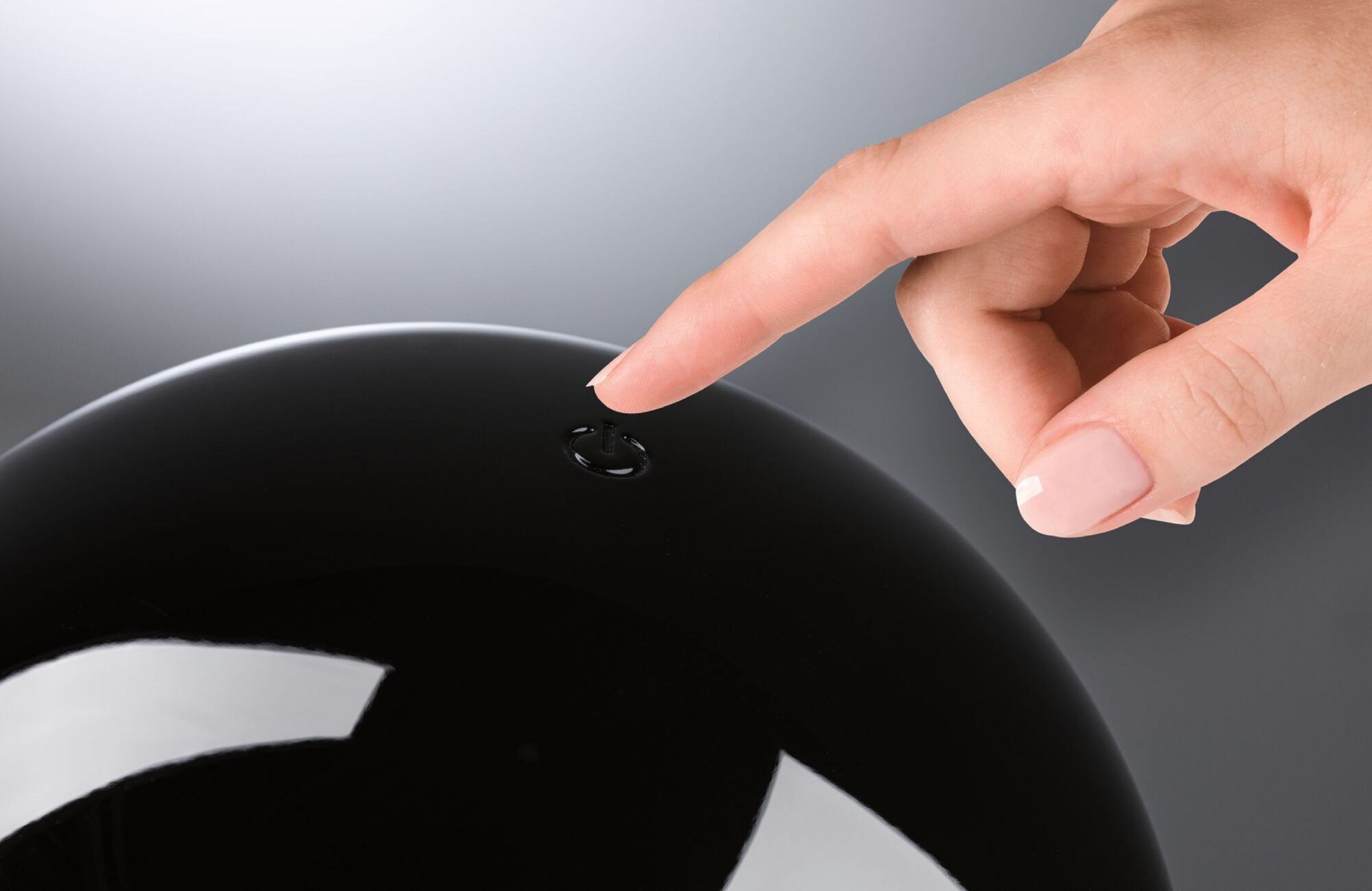 Zbliżenie palca dotykającego czarnego, zaokrąglonego przedmiotu. Tło jest rozmyte.
