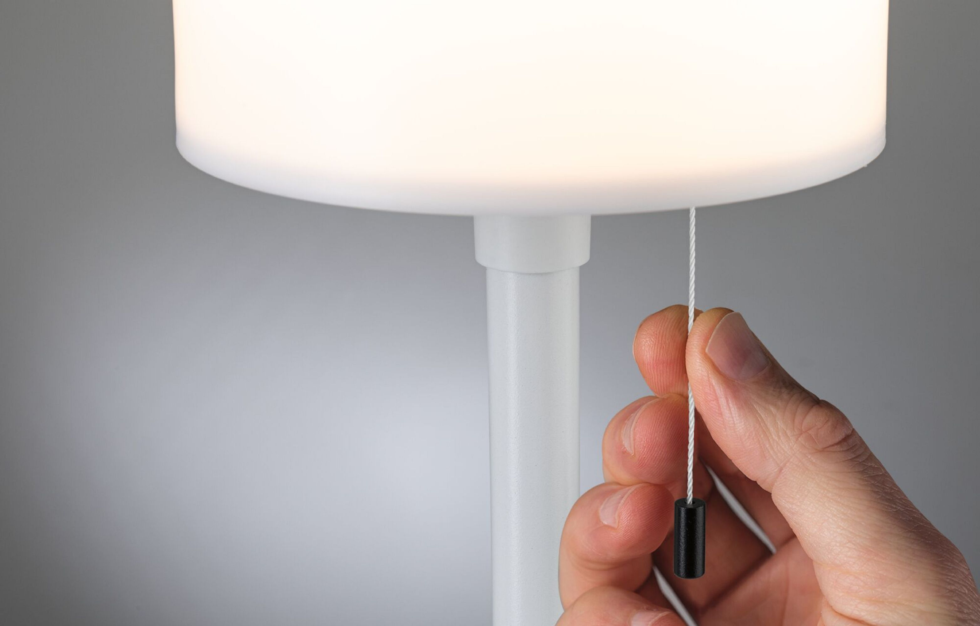 Ręka pociąga za sznurek białej lampy, aby ją włączyć, widok z bliska.