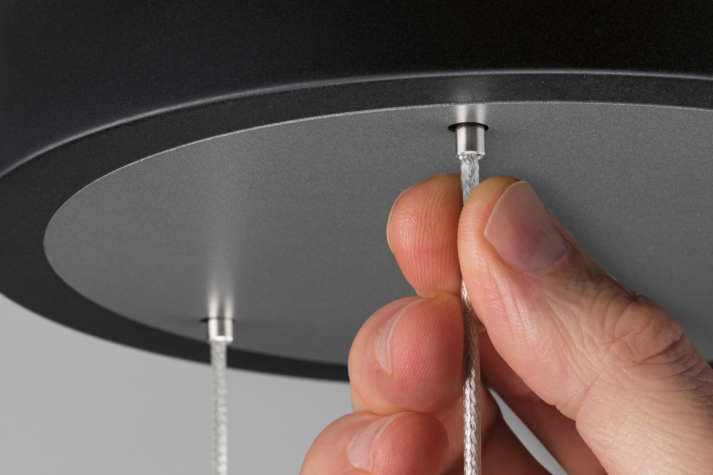 Ręka mocuje kabel do górnej części nowoczesnej czarno-srebrnej lampy wiszącej.