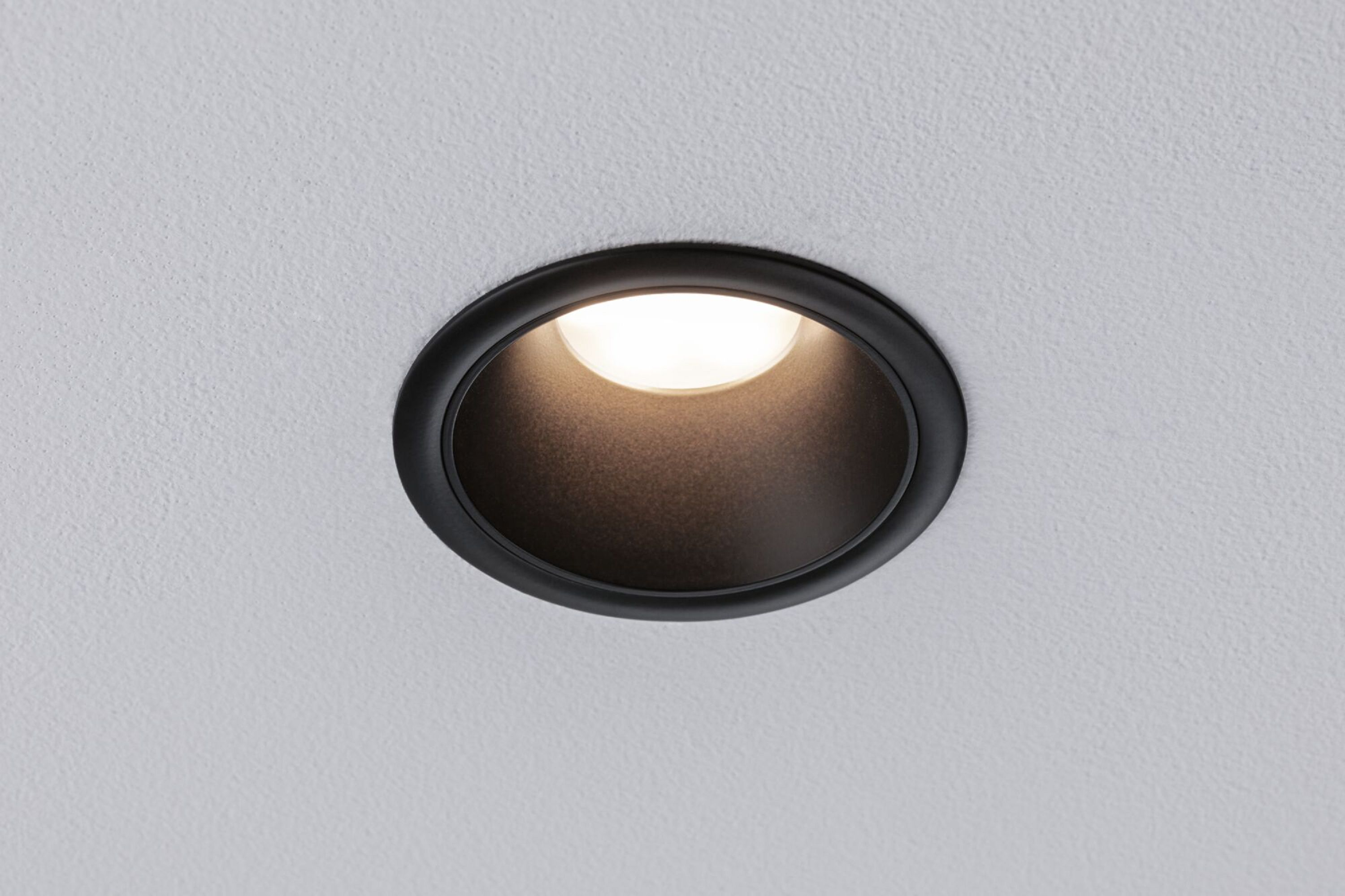 Czarna oprawa wpuszczana w biały sufit, emitująca miękkie światło.