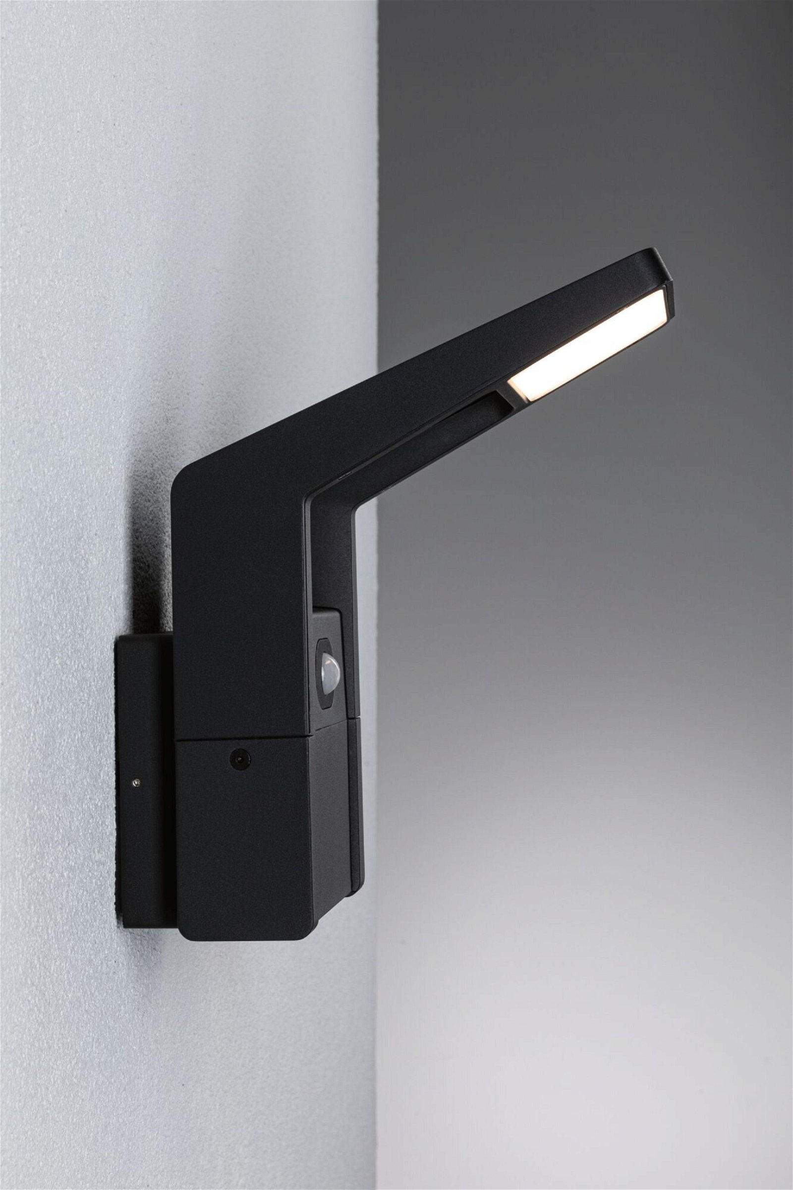 Czarna zewnętrzna lampa ścienna z czujnikiem ruchu, zamontowana na jasnej ścianie.