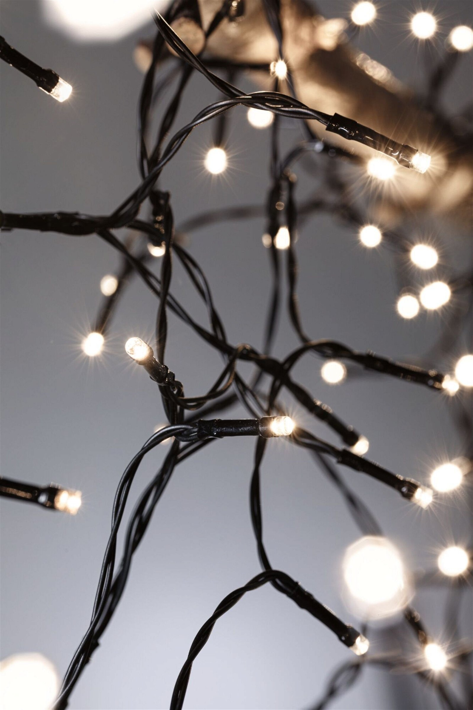 Szereg białych świateł na czarnych przewodach. Niektóre światła ostre, inne rozmyte. Szare tło.