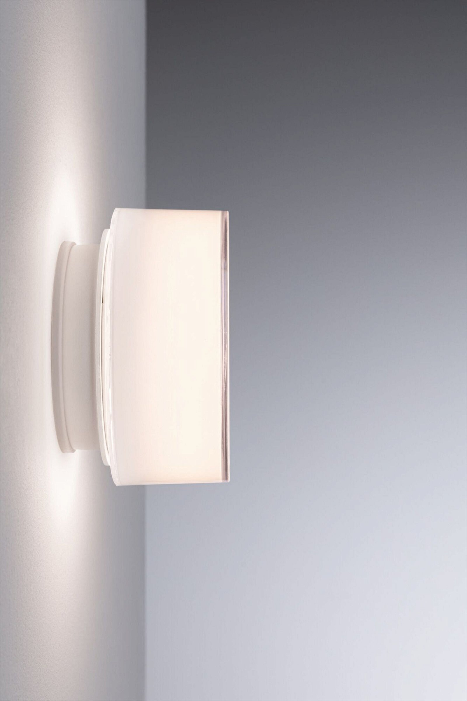 Eine weiße Wandleuchte strahlt Licht aus. Die Lampe ist rechteckig mit matter Front.