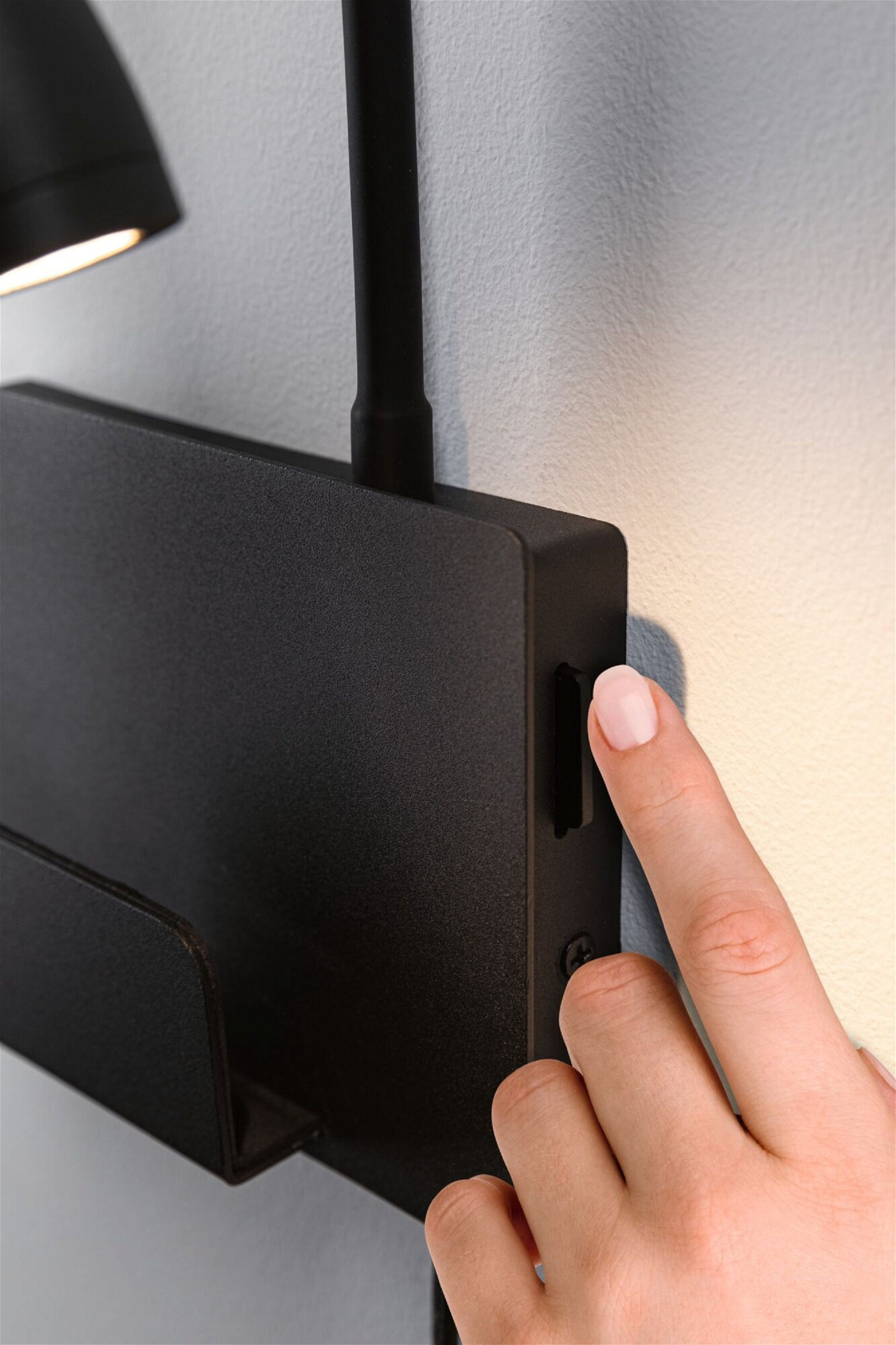 Dłoń włącza czarną lampę ścienną, widok z bliska.