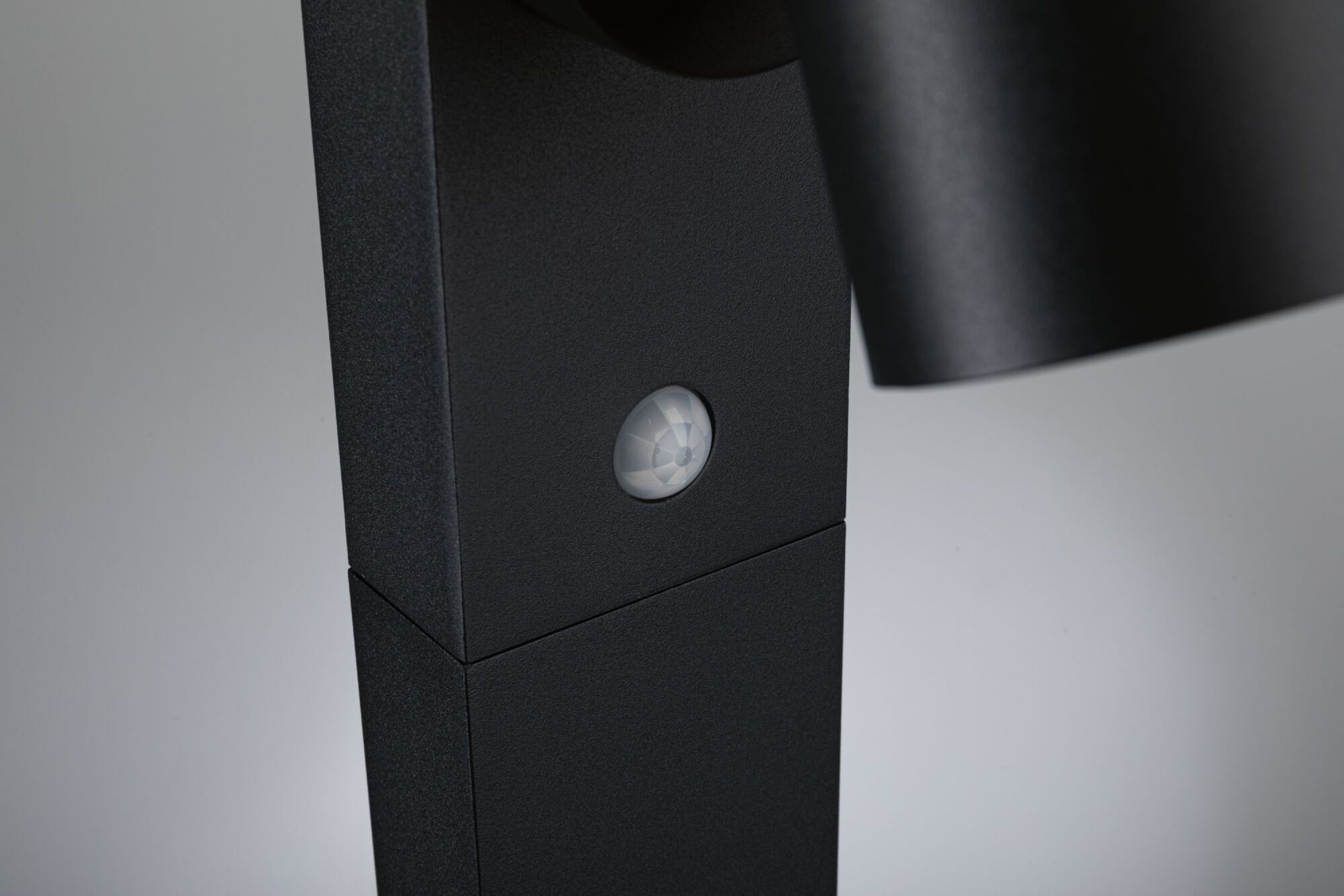 Czarny słupek oświetleniowy z czujnikiem ruchu i czarną lampą, z rozmytym tłem.