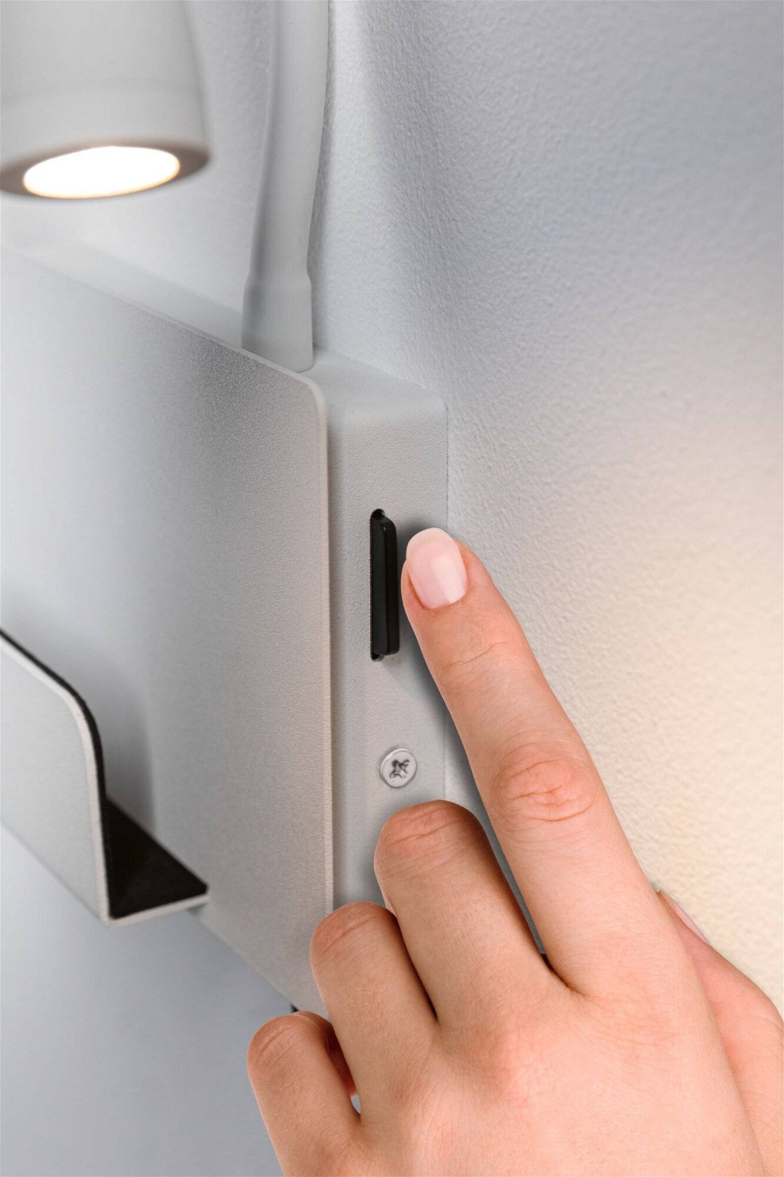 Palec wkłada kartę pamięci do gniazda karty urządzenia, w pobliżu lampy ściennej.