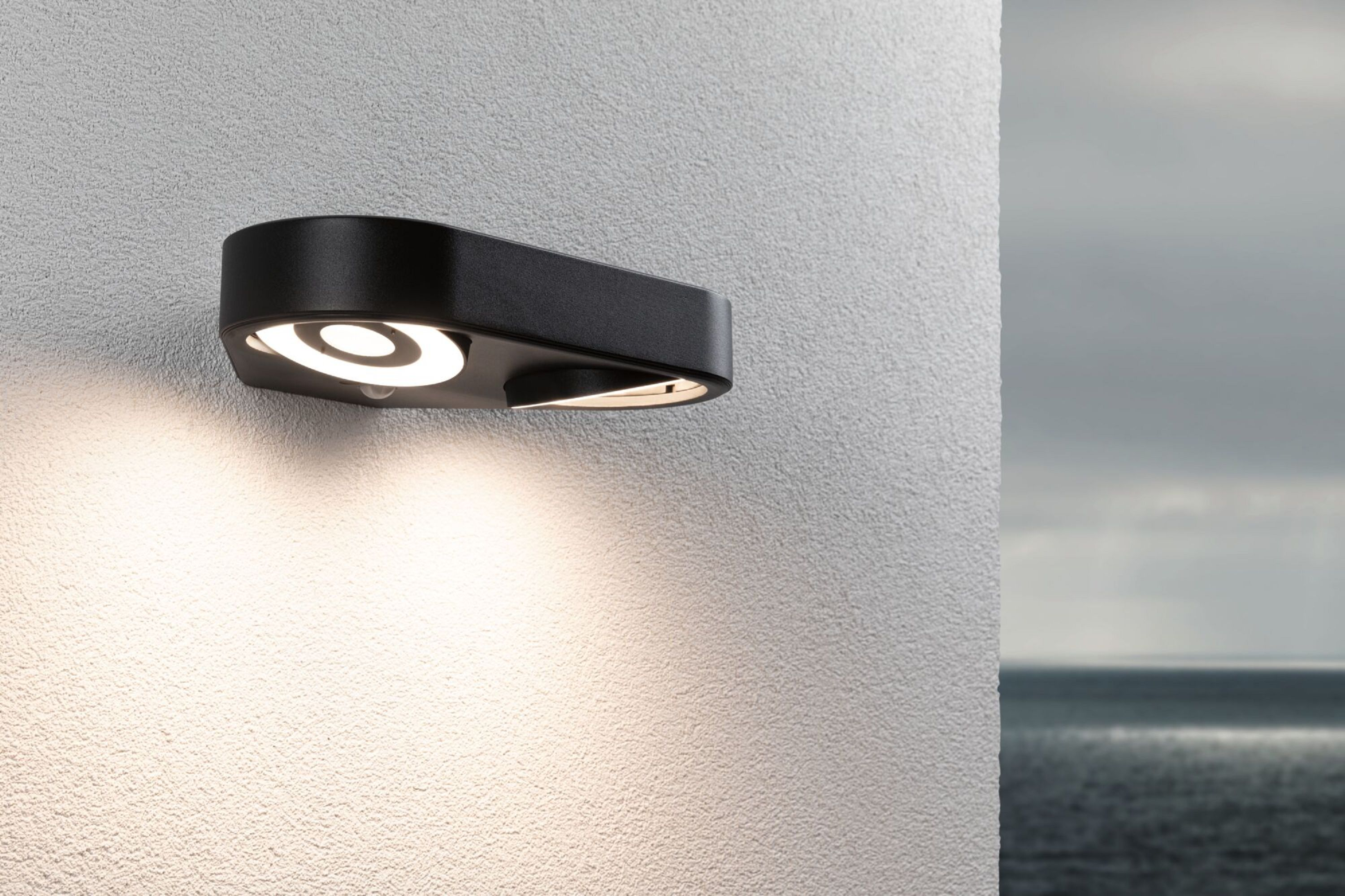 Czarna lampa ścienna z białym światłem skierowanym w dół. Biała ściana i rozmyte tło.