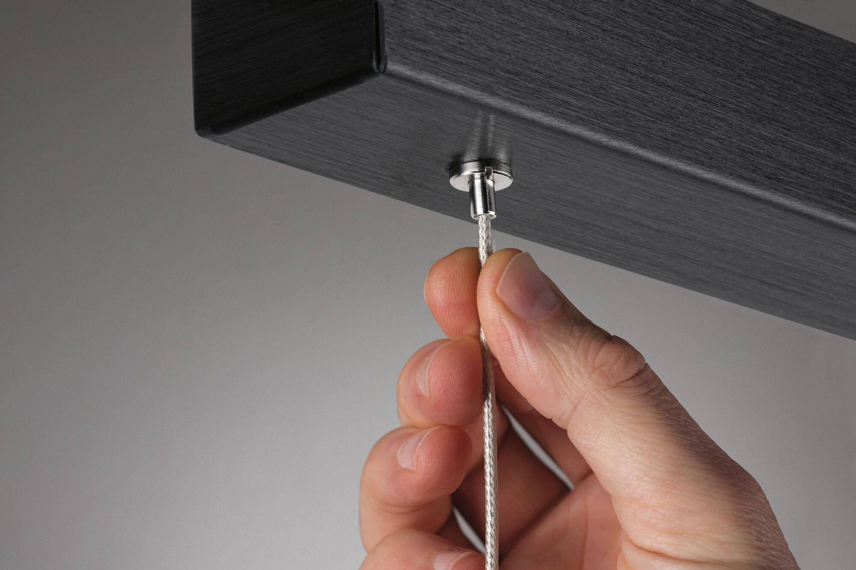 Eine Hand, die ein dünnes Metallkabel hält, das mit einer schwarzen, metallischen Struktur verbunden ist.