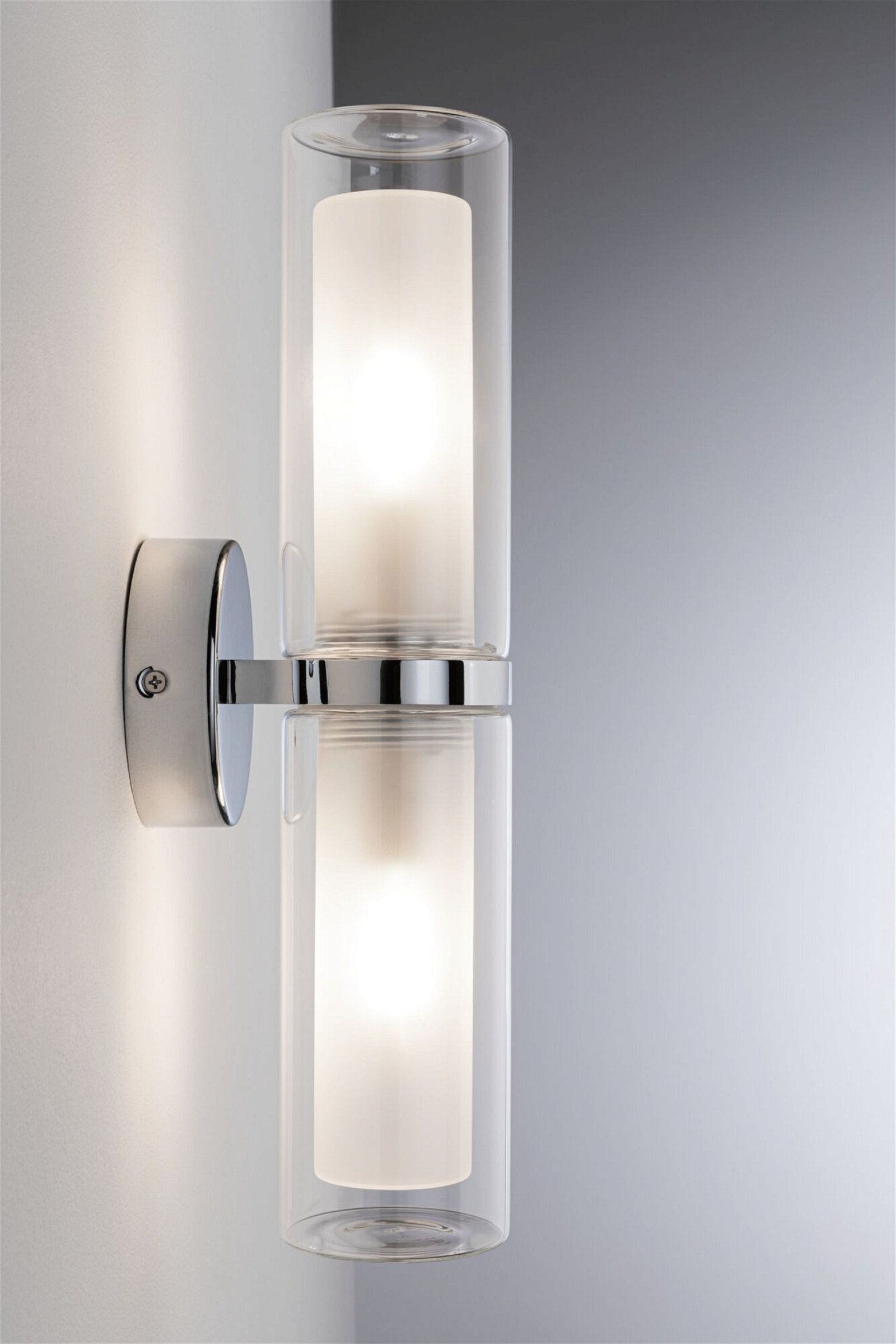 Lampa ścienna z dwoma przezroczystymi szklanymi cylindrami, chromowana podstawa, podświetlana.