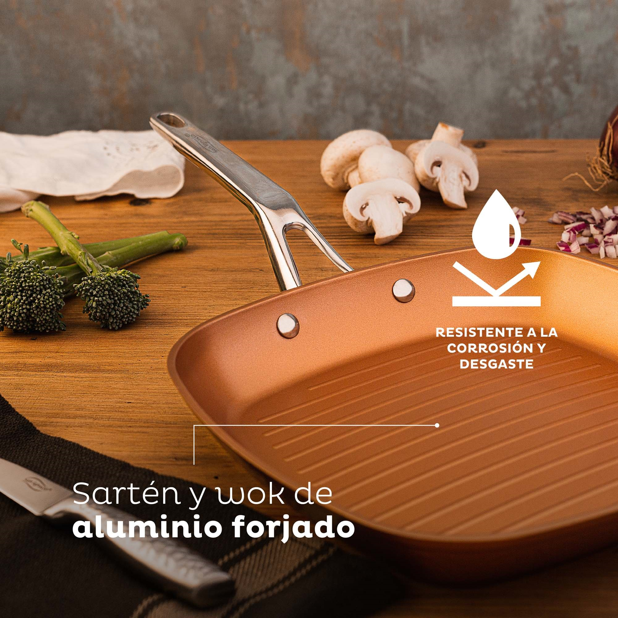 Sartén parrilla color cobre con comida sobre madera. Champiñones y brócoli visibles.