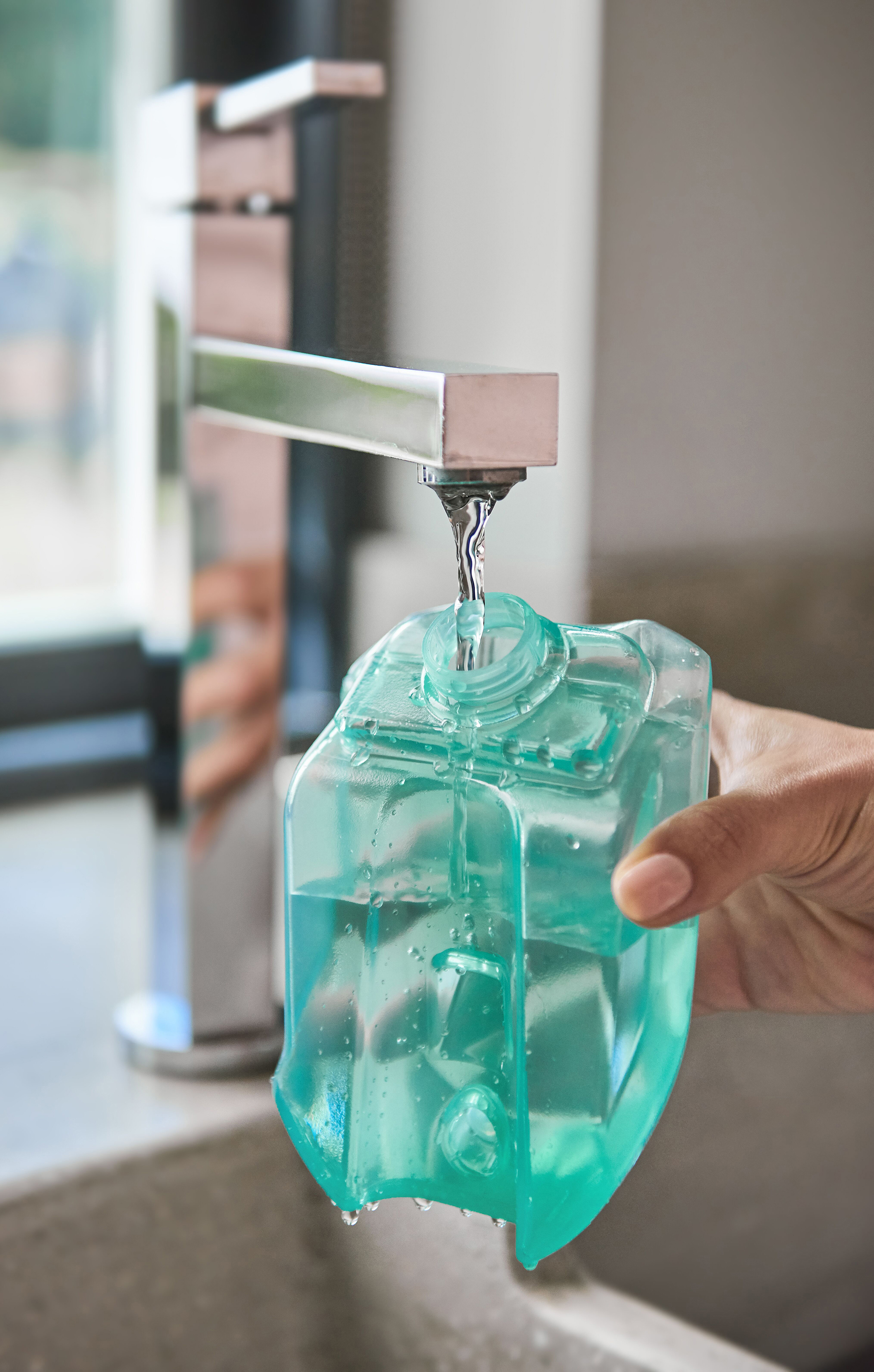 Ein Wasserhahn, der einen durchsichtigen, türkisfarbenen Wasserbehälter in der Küche füllt.