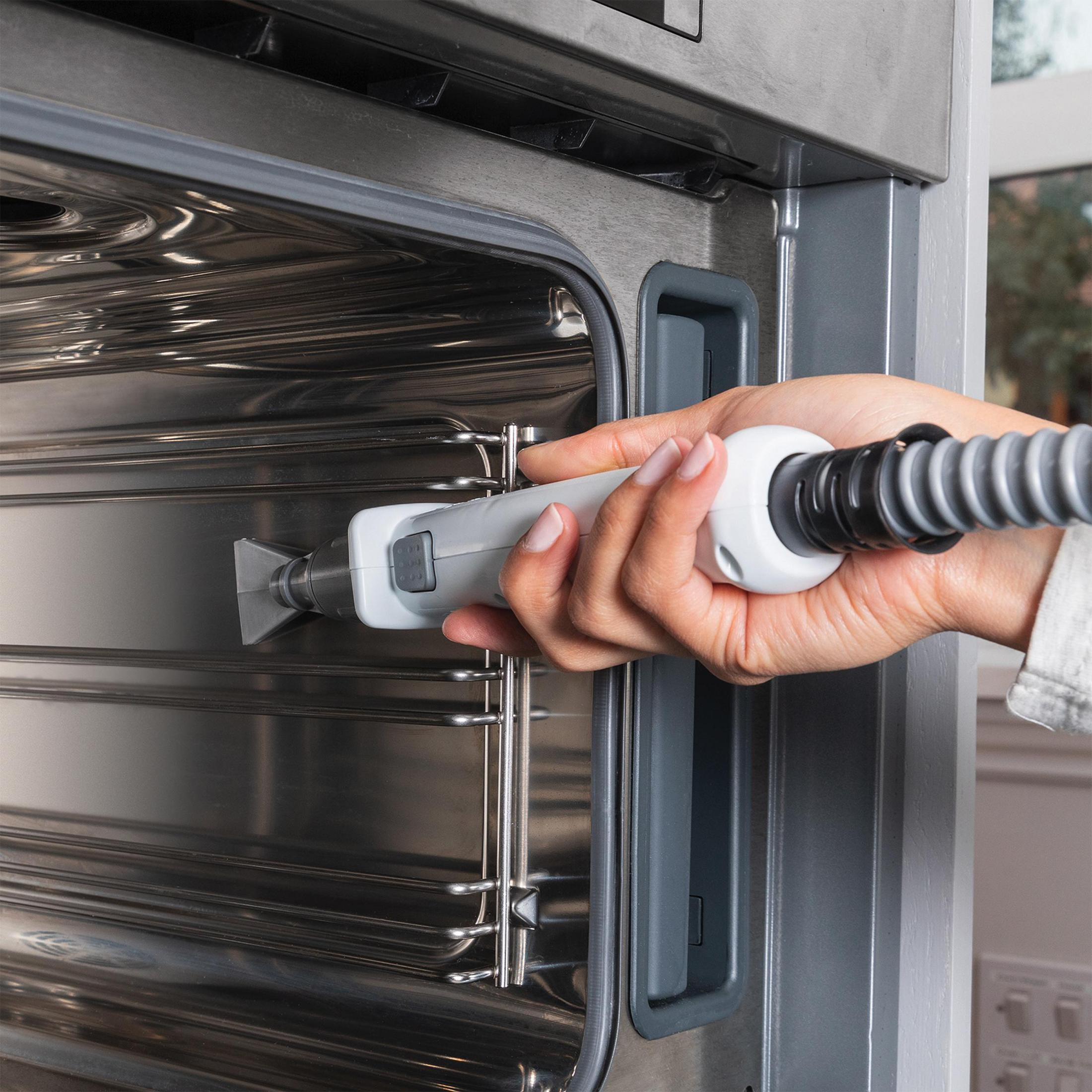 Ręka trzymająca narzędzie do czyszczenia wewnątrz piekarnika ze stali nierdzewnej.