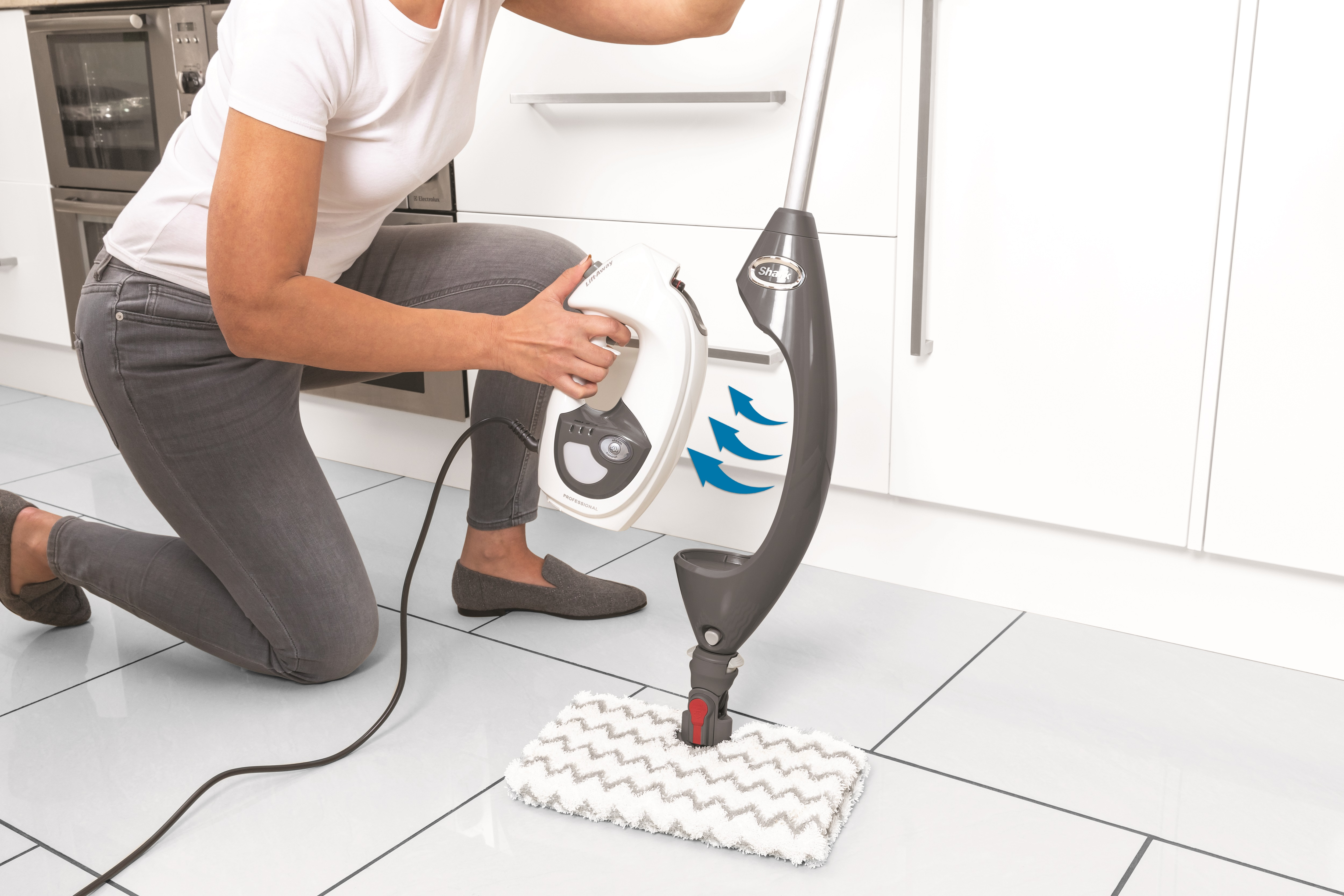 A person is cleaning the floor with a steam mop. There are white tiles.