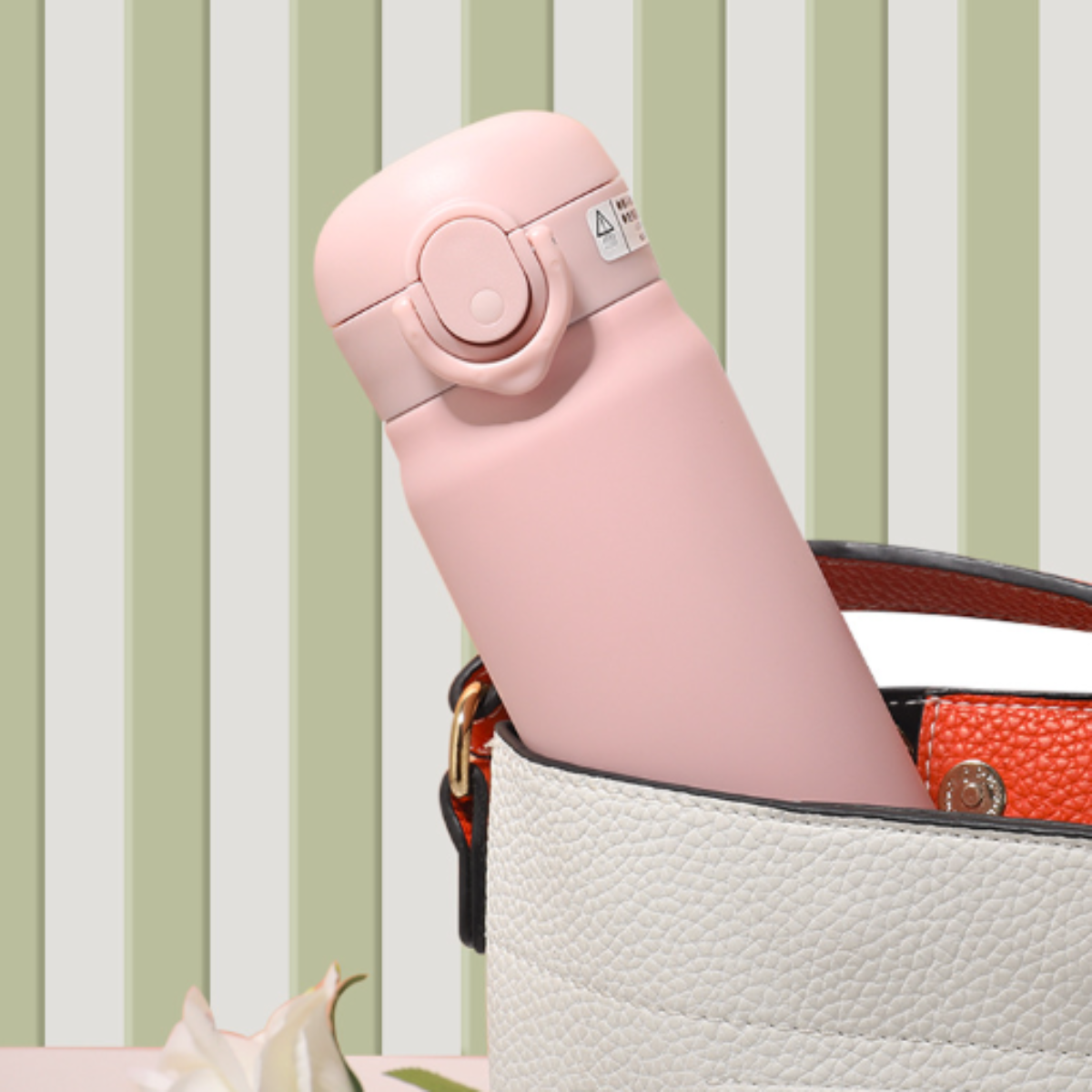 Eine rosa Thermoskanne in einer weißen Handtasche. Der Hintergrund hat grüne und weiße Streifen.