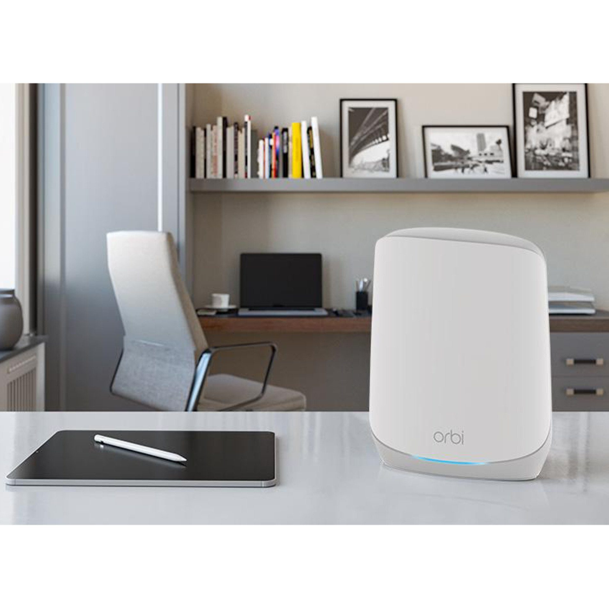 Un router bianco su una scrivania con tablet e stilo. Sullo sfondo, una scrivania con laptop, sedia e arte incorniciata.