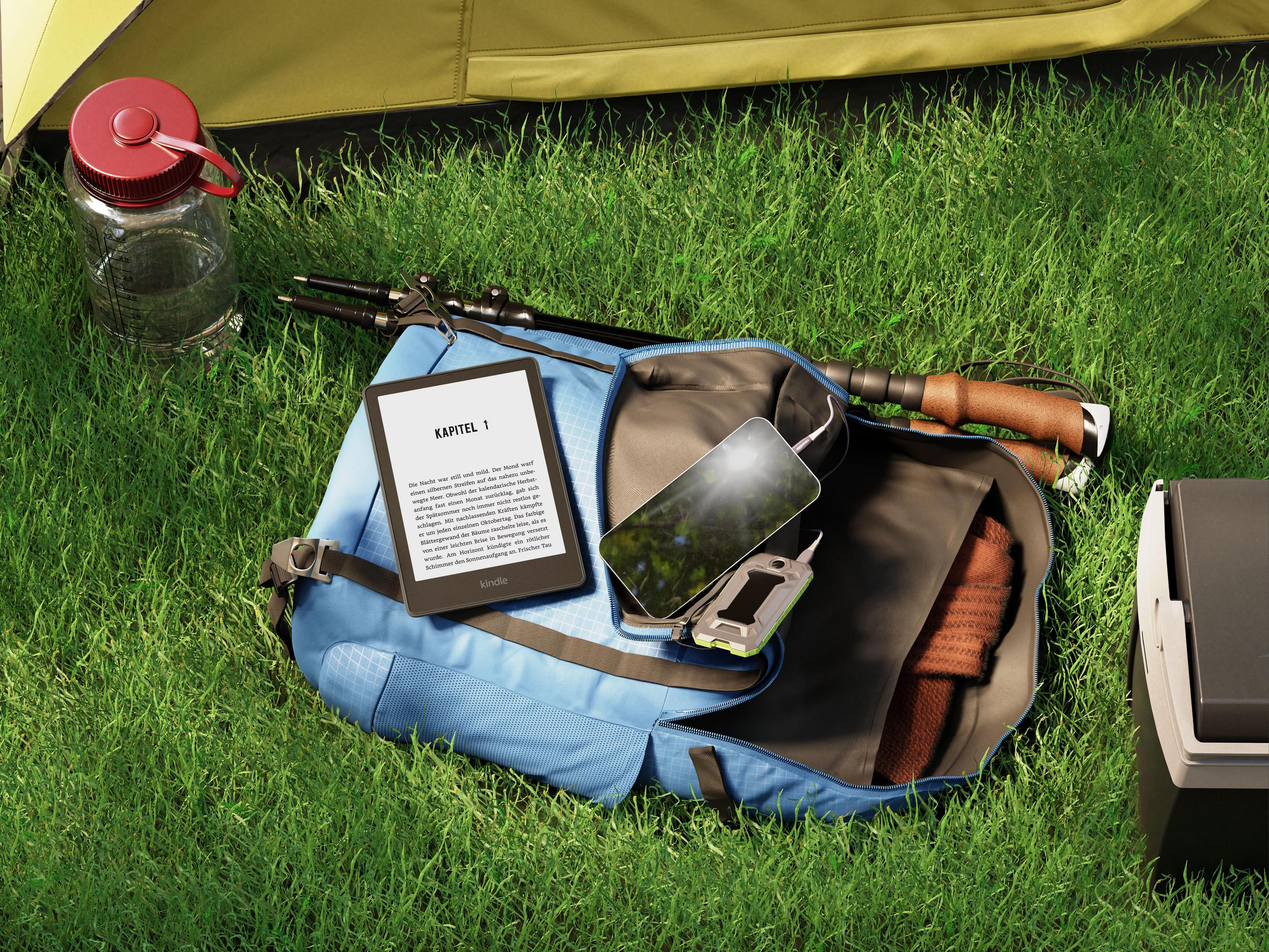 Rucksack auf Gras. Kindle, Telefon laden, Wasserflasche und Trekkingstöcke in der Nähe.