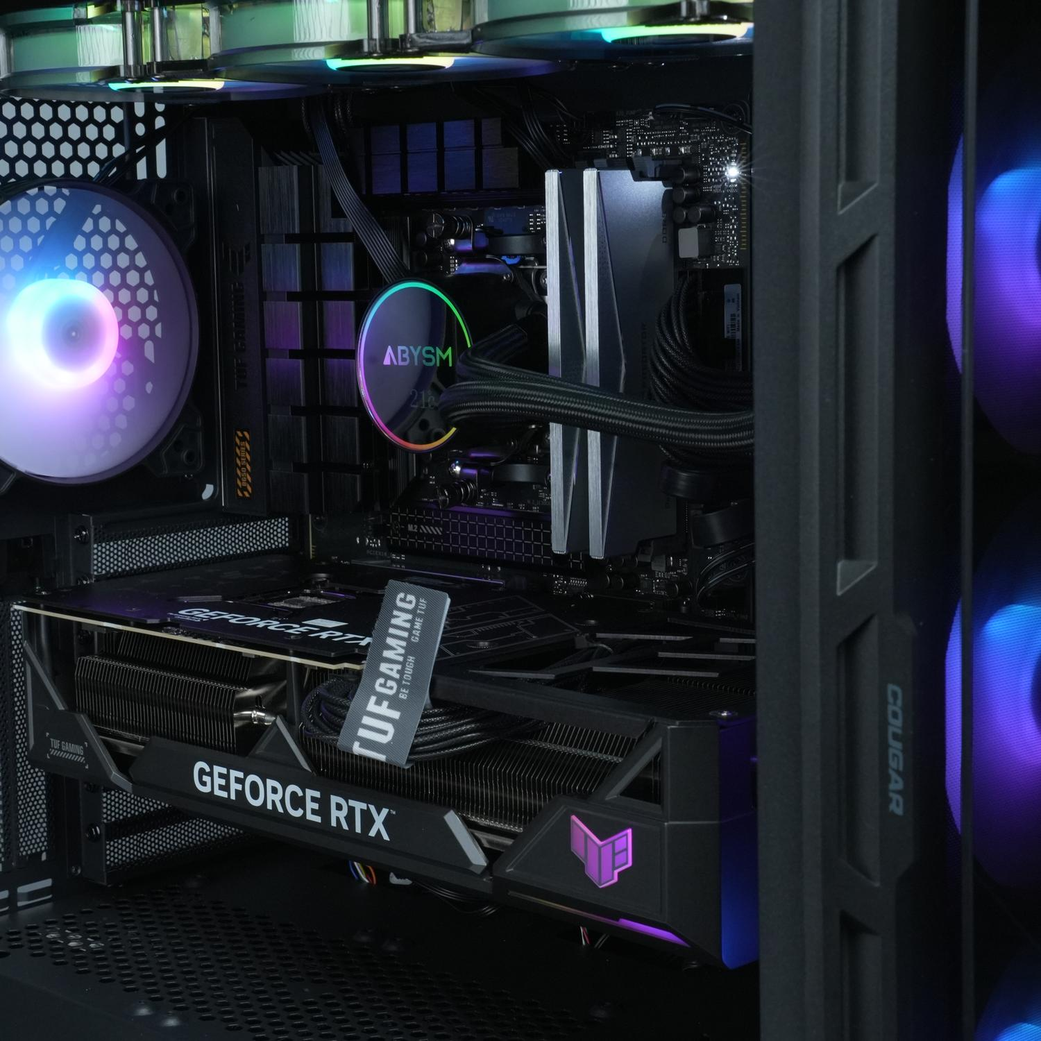 Interior de la caja de PC: GPU, enfriador de CPU, ventiladores con luces moradas y azules, y una pegatina TUF Gaming.