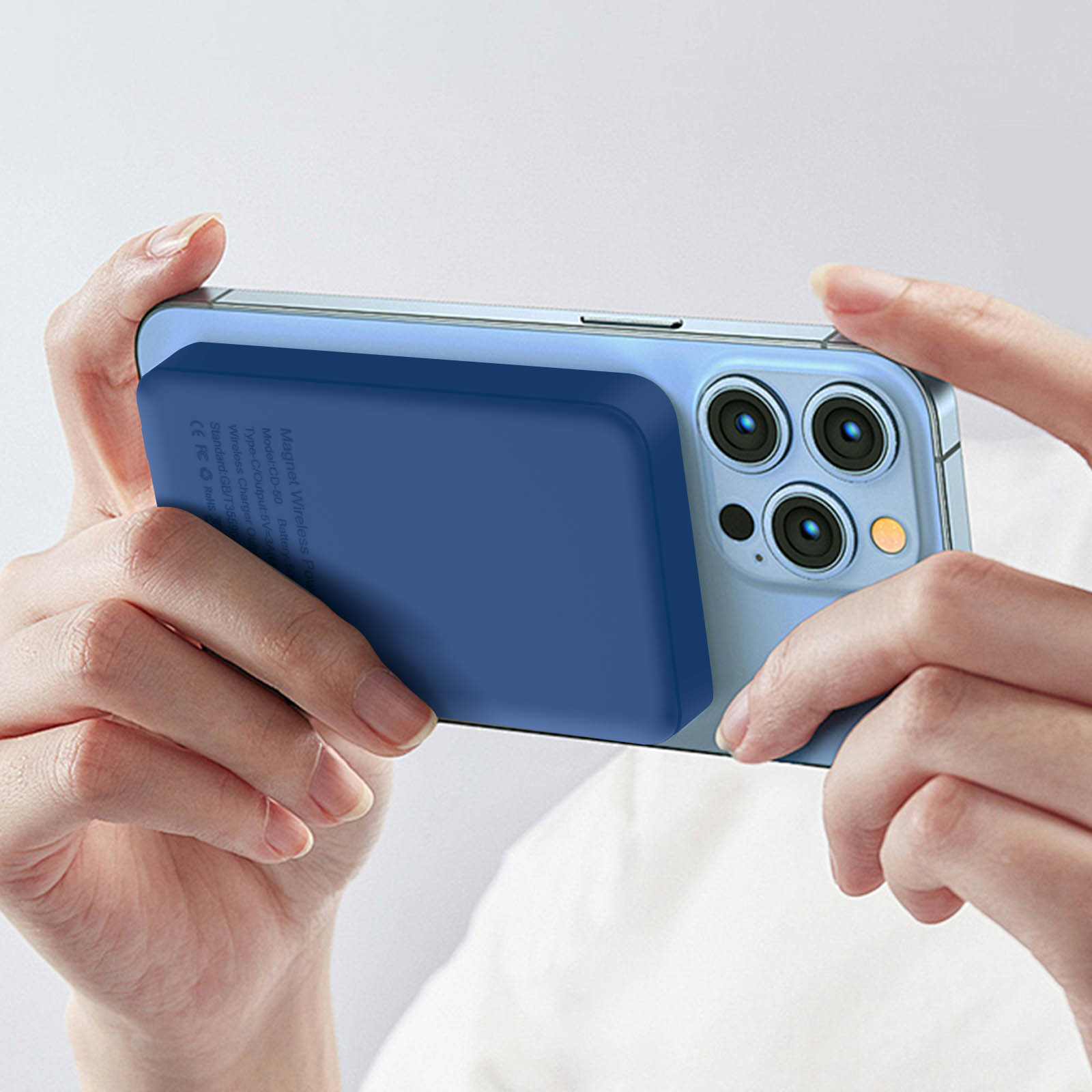 Manos sosteniendo un teléfono azul con una plataforma de carga adjunta. El teléfono se sostiene horizontalmente.
