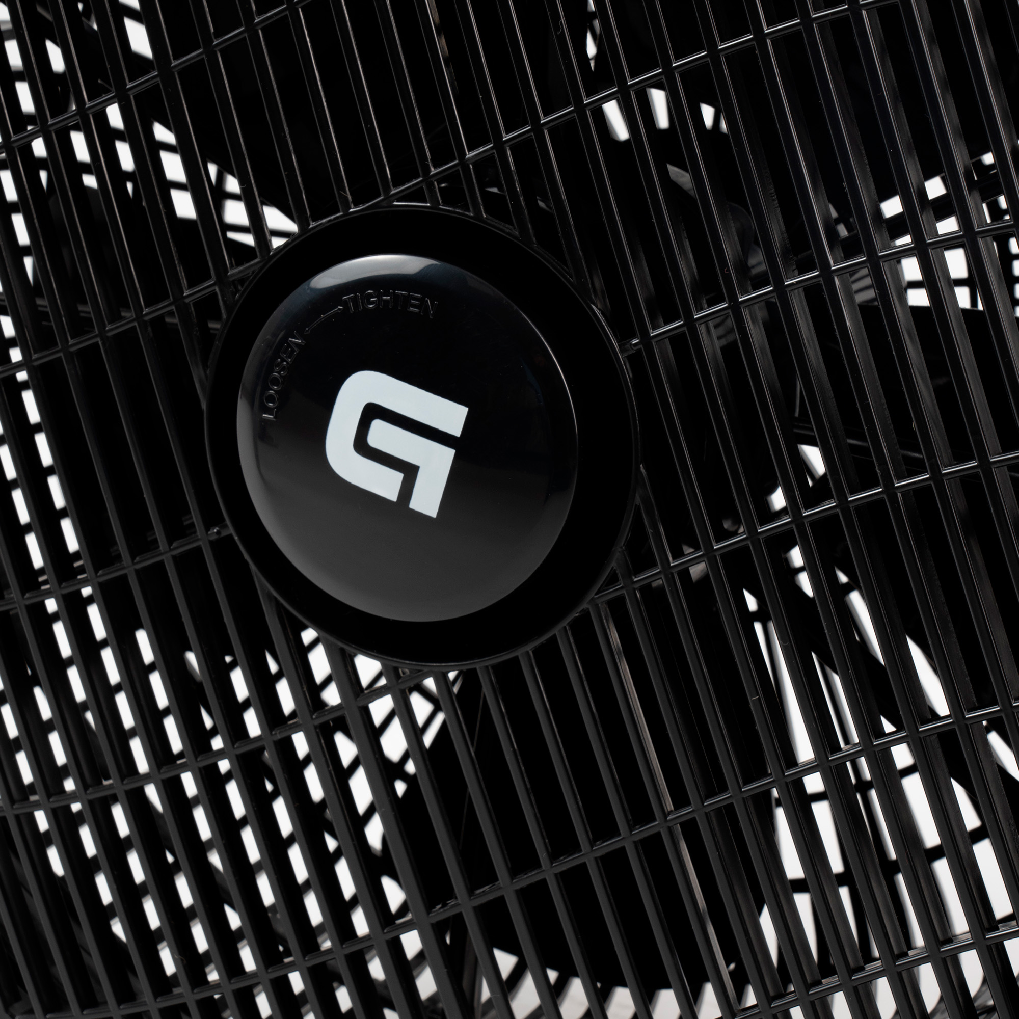 Un ventilador negro con un logotipo circular central y una rejilla metálica. La rejilla tiene un patrón de rejilla.