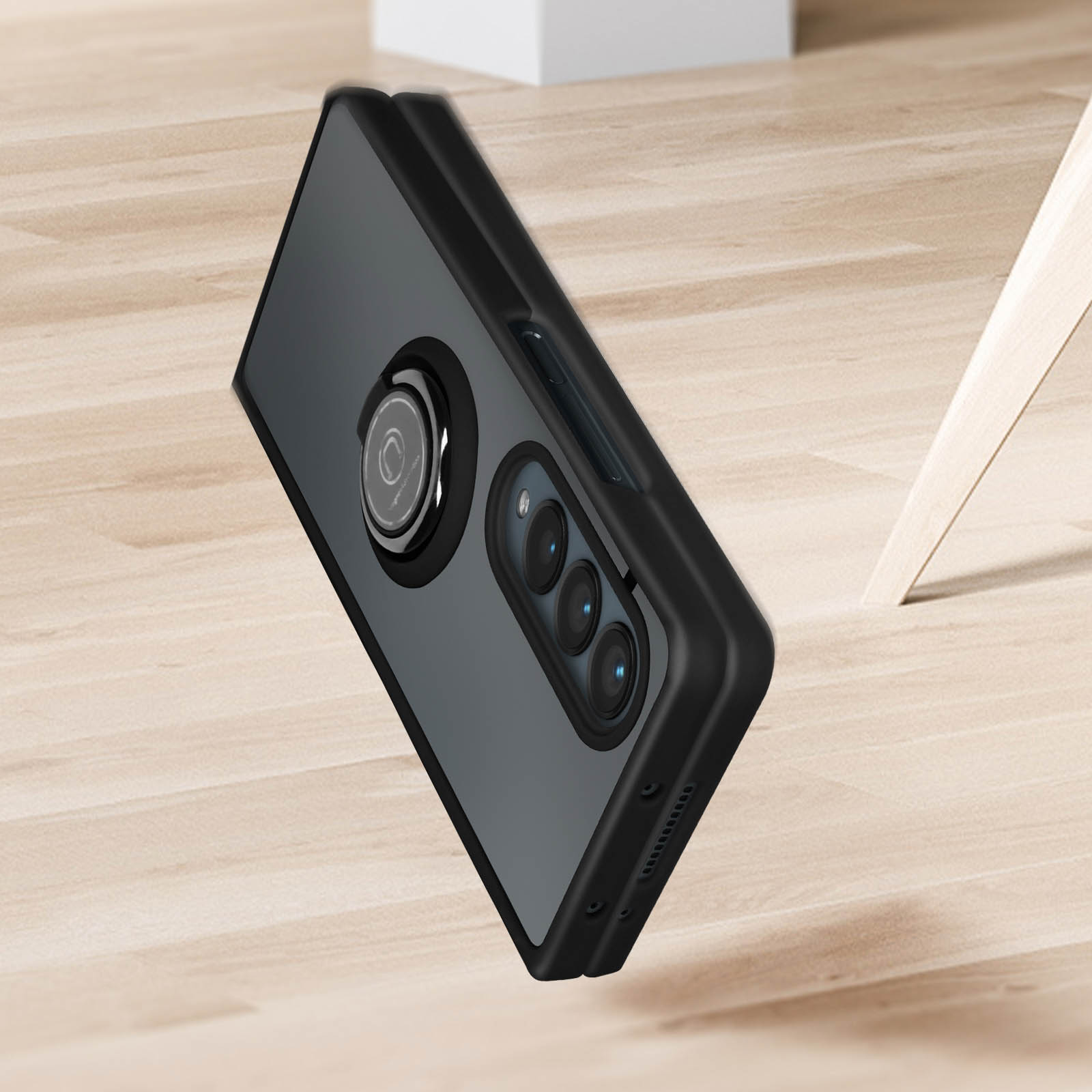 Custodia nera per telefono con anello e tre lenti della fotocamera su superficie in legno.