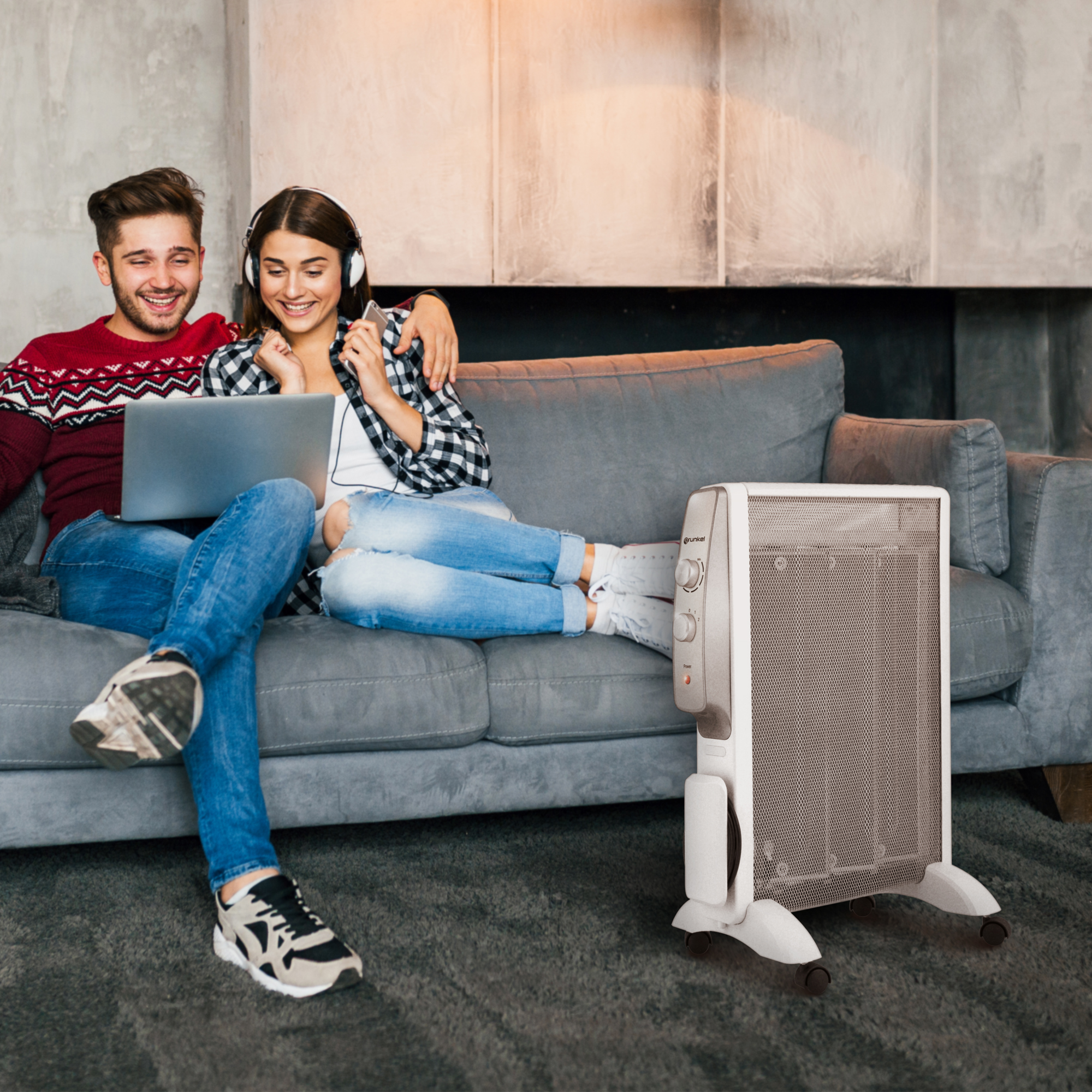 Pareja en sofá con portátil, radiador a su lado.