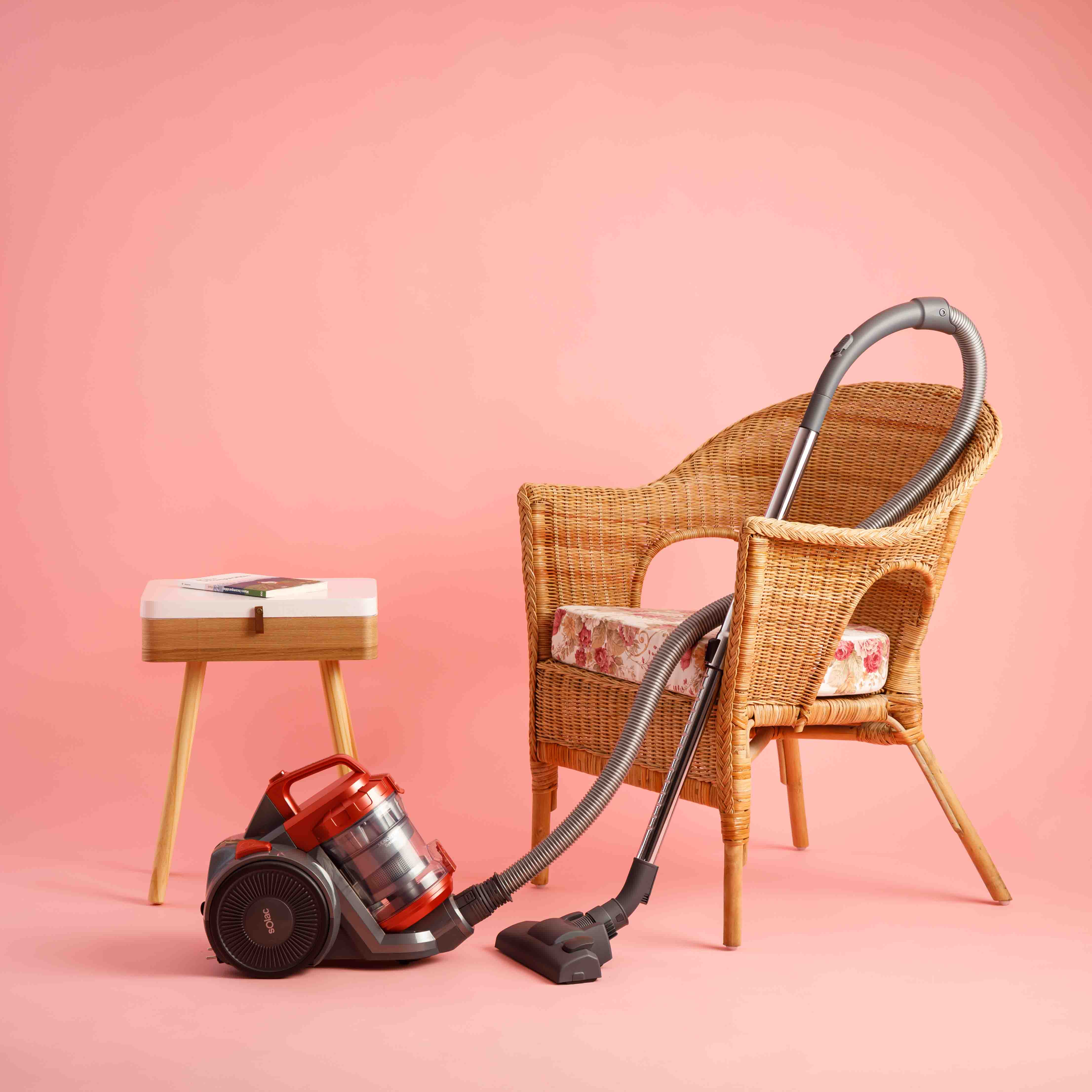 Odkurzacz i krzesło na różowym tle. Po lewej stronie mały stolik.