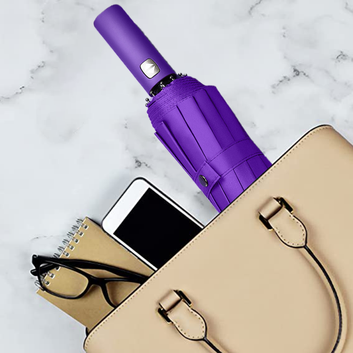Beige Handtasche mit lila Regenschirm, Smartphone, Brille und Notizbuch auf Marmor.