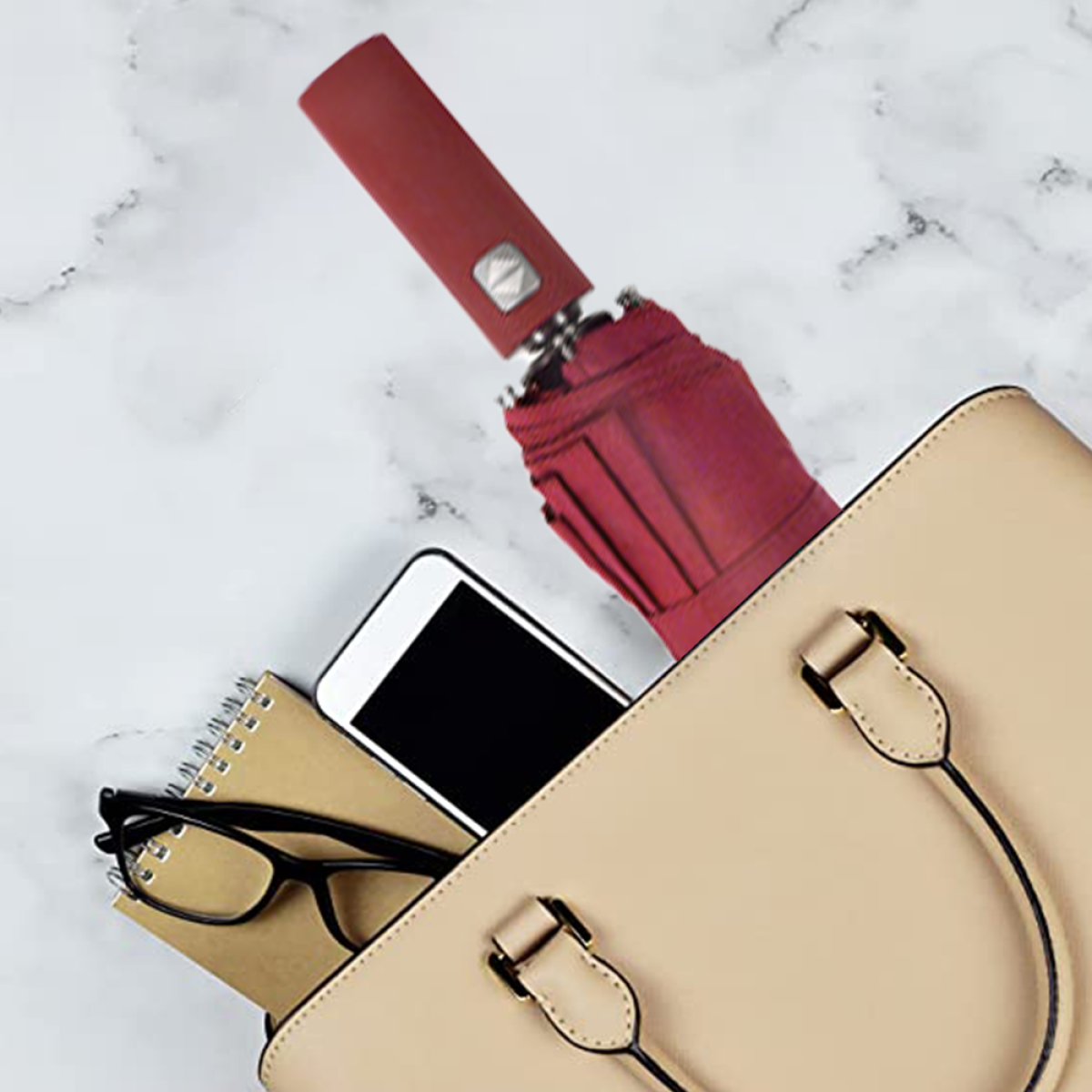 Eine beige Handtasche mit einem Regenschirm, einem Telefon, einem Notizbuch und einer Brille.