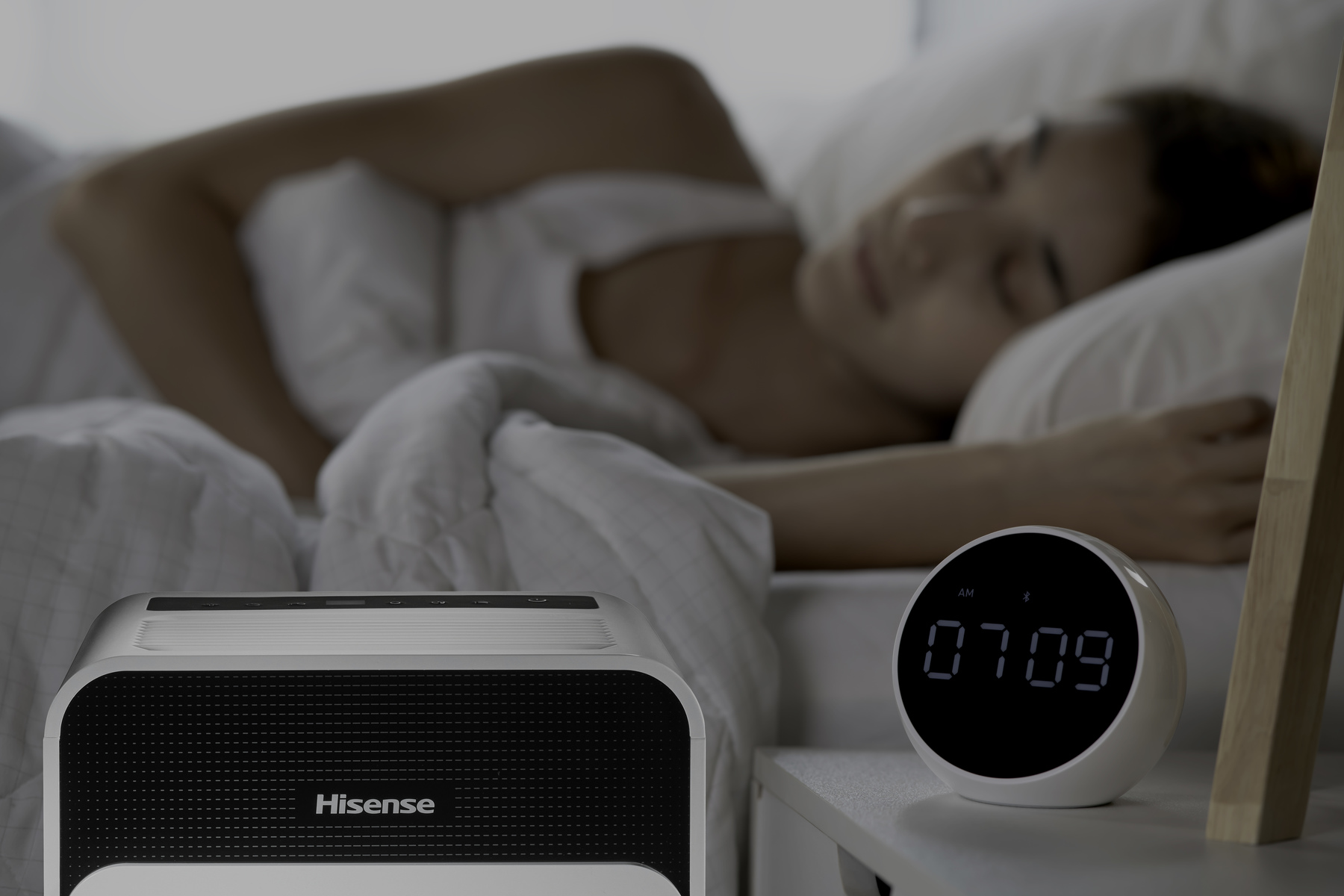 Scena sypialni. Śpiąca kobieta, biały głośnik Hisense i cyfrowy budzik.