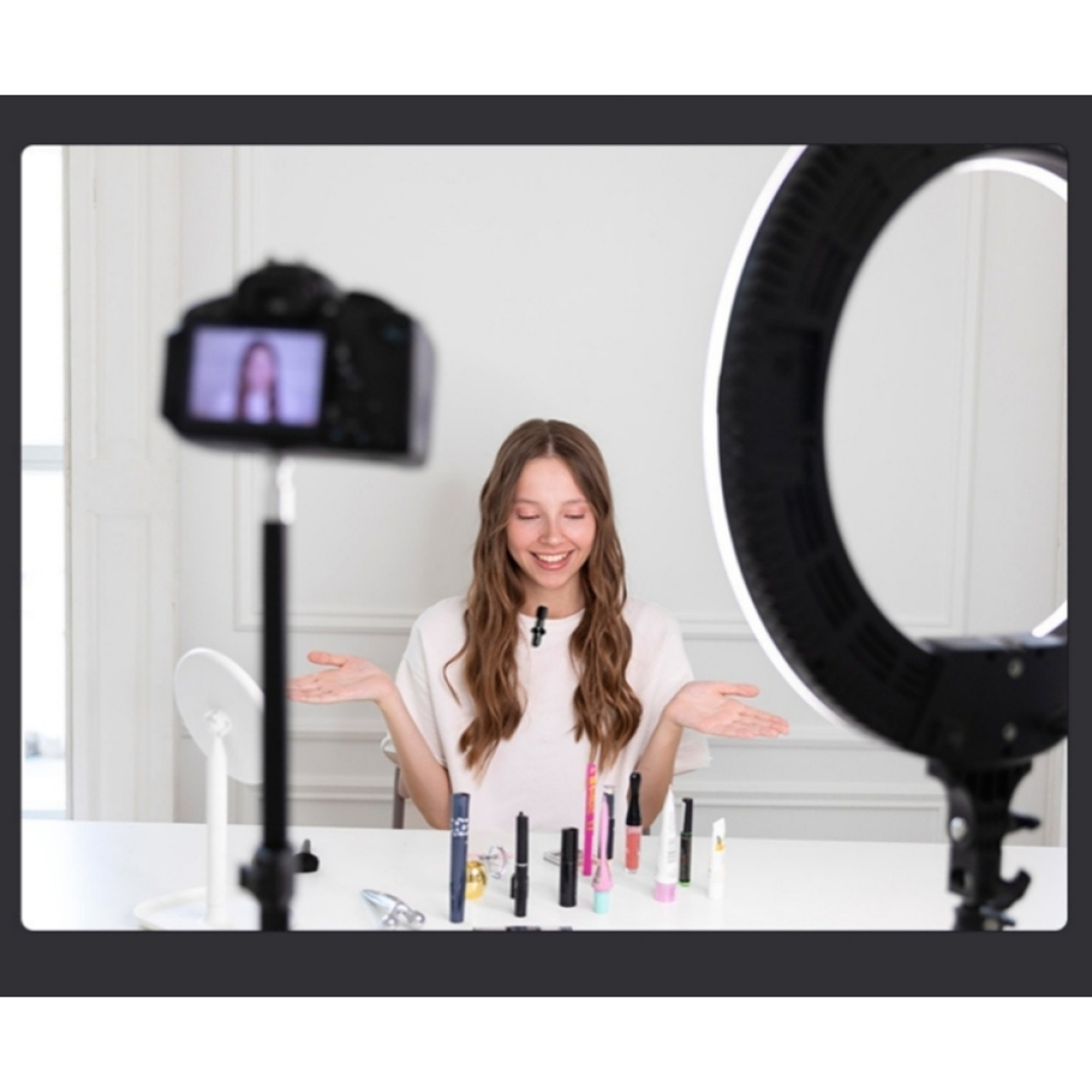Eine Frau filmt ein Make-up-Tutorial. Sie lächelt und hat Make-up-Produkte auf dem Tisch.