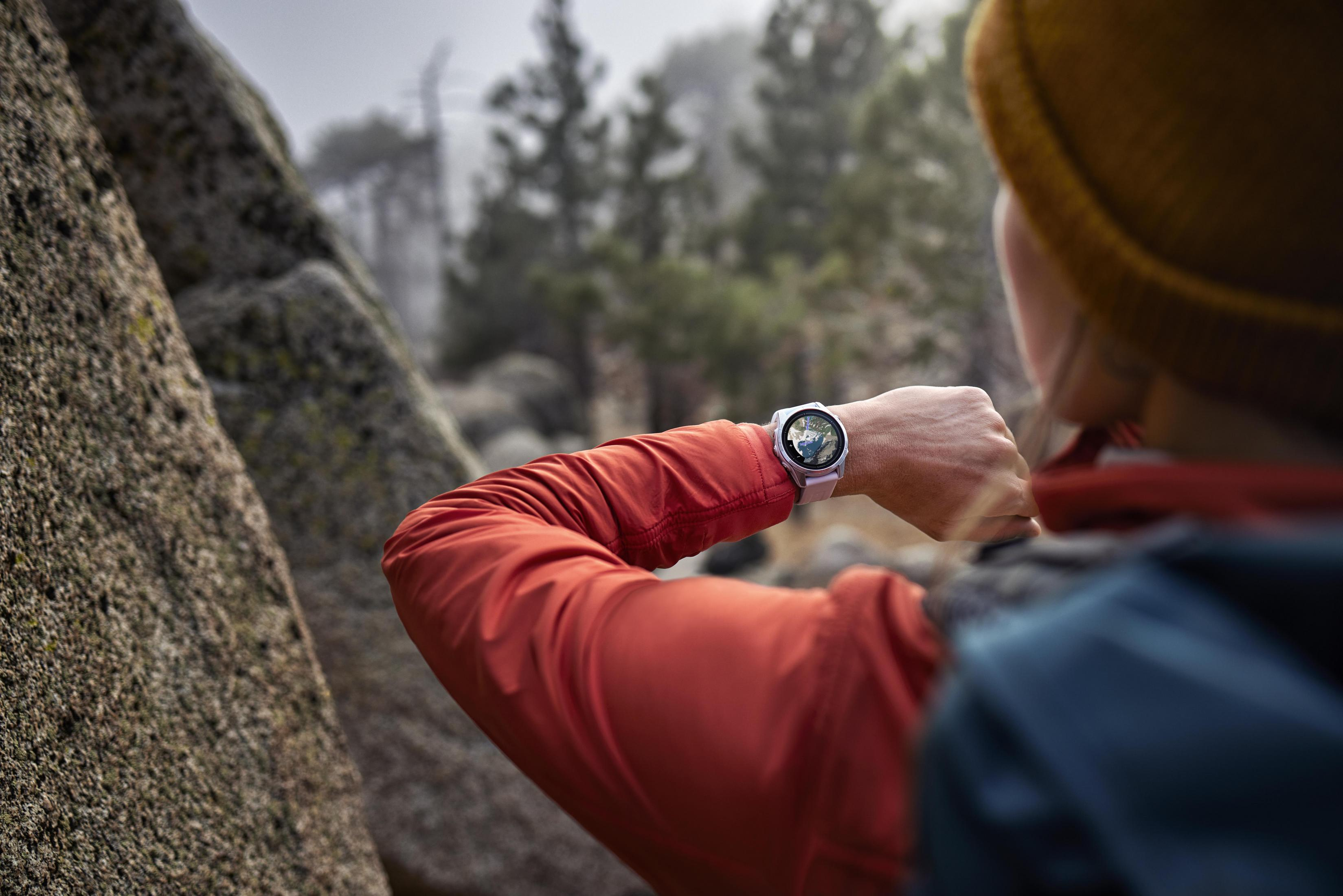 Kobieta nosząca zegarek na nadgarstku, patrząca na niego, stojąc w pobliżu skał i drzew.